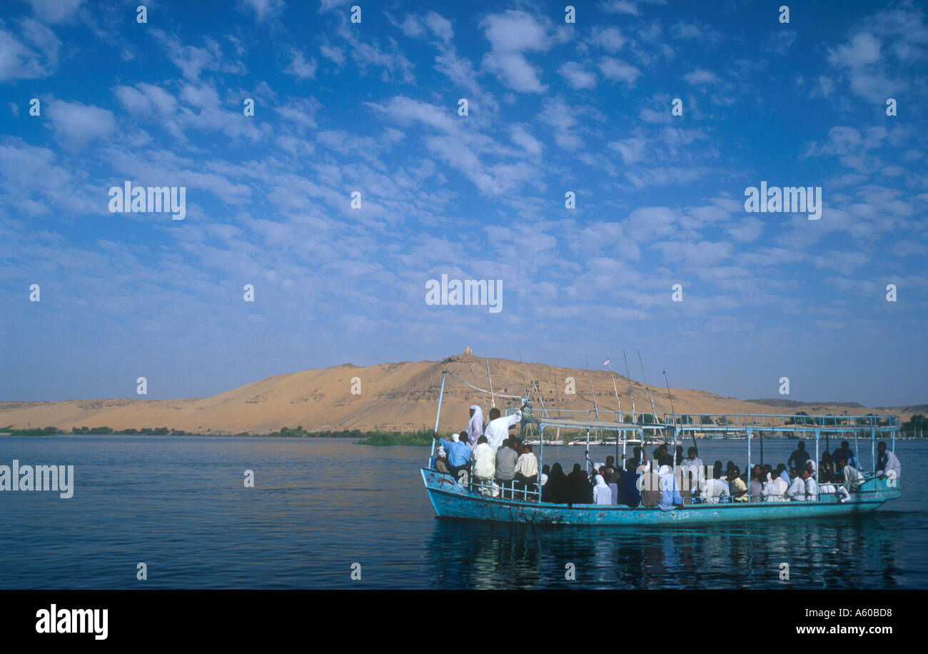 Egitto Alto Egitto Aswan Qubbet el Hawa e le tombe dei nobili con stato caricato un traghetto passeggeri passato a vela sul fiume Nilo Foto Stock