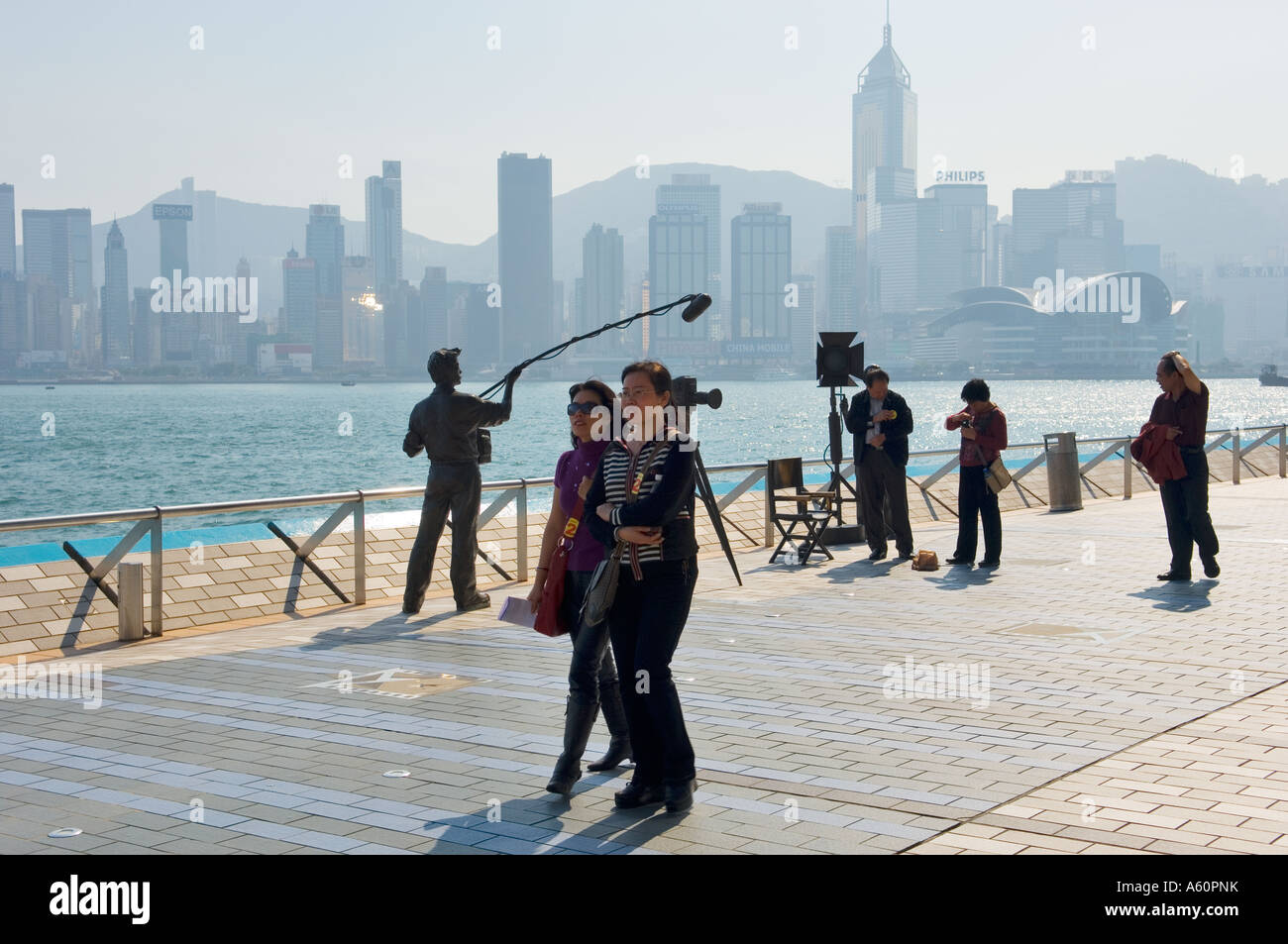 Turisti e set cinematografico statue con Isola di Hong Kong con il Victoria Harbour dietro. Sul Viale delle Stelle promenade, Kowloon, Cina Foto Stock