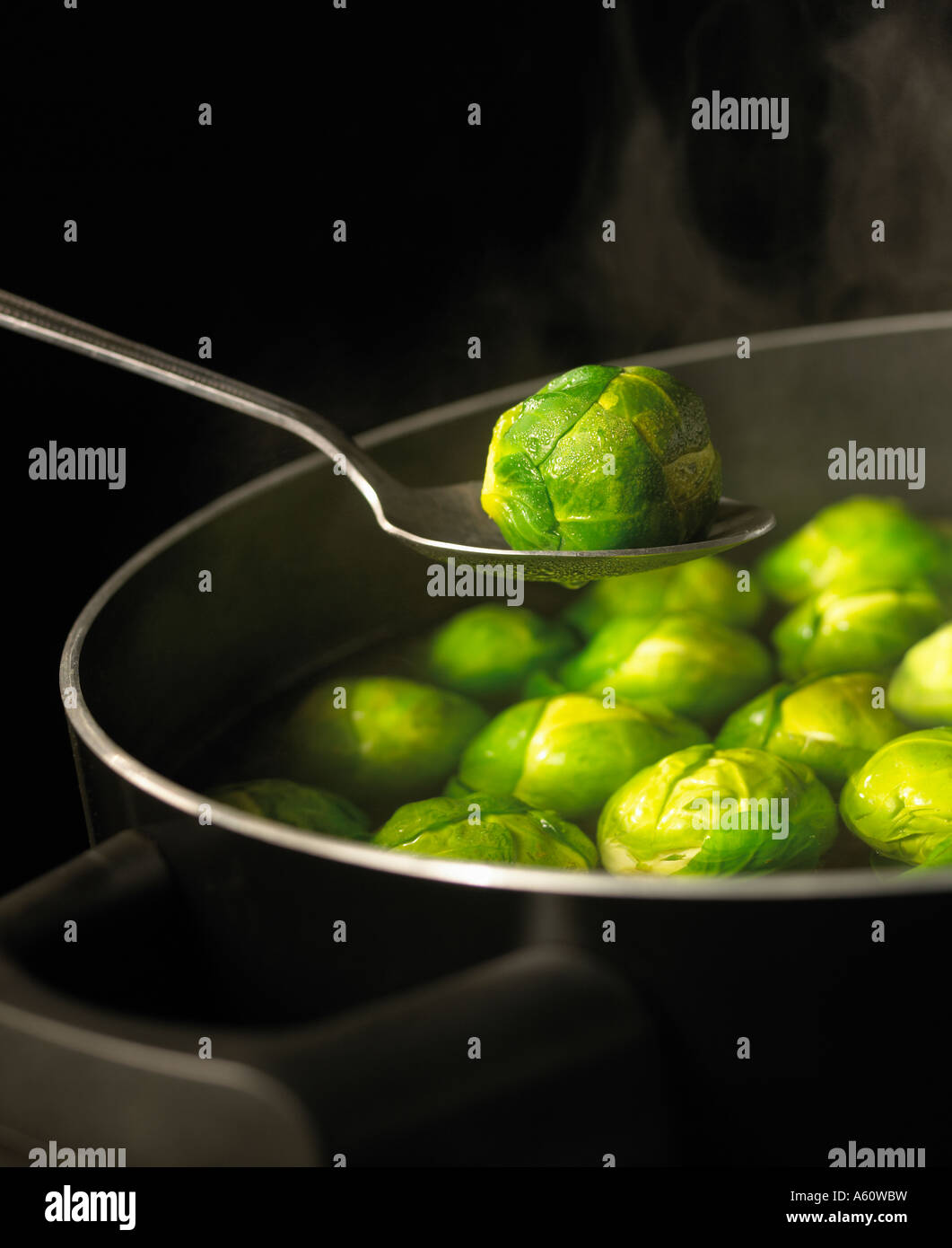 Cucchiaio HOLDING germoglio di Bruxelles sulla pentola di acqua bollente piena di germogli con vapore ascendente SIMMERING sul fornello a gas Foto Stock