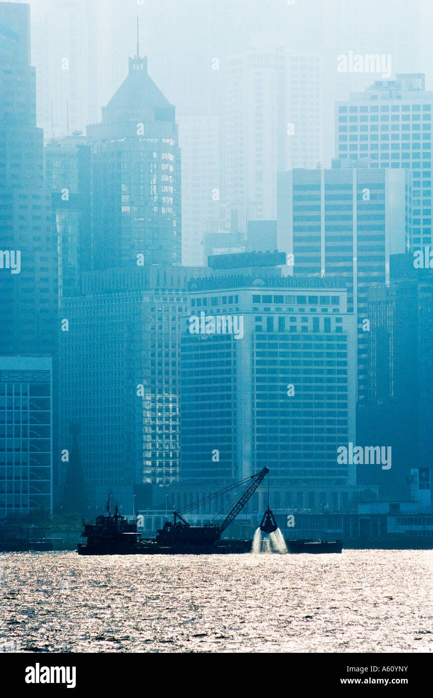Draga barca limo di sollevamento dal Porto di Hong Kong Harbour con sfondo dell'Isola di Hong Kong per il distretto centrale alte torri Foto Stock
