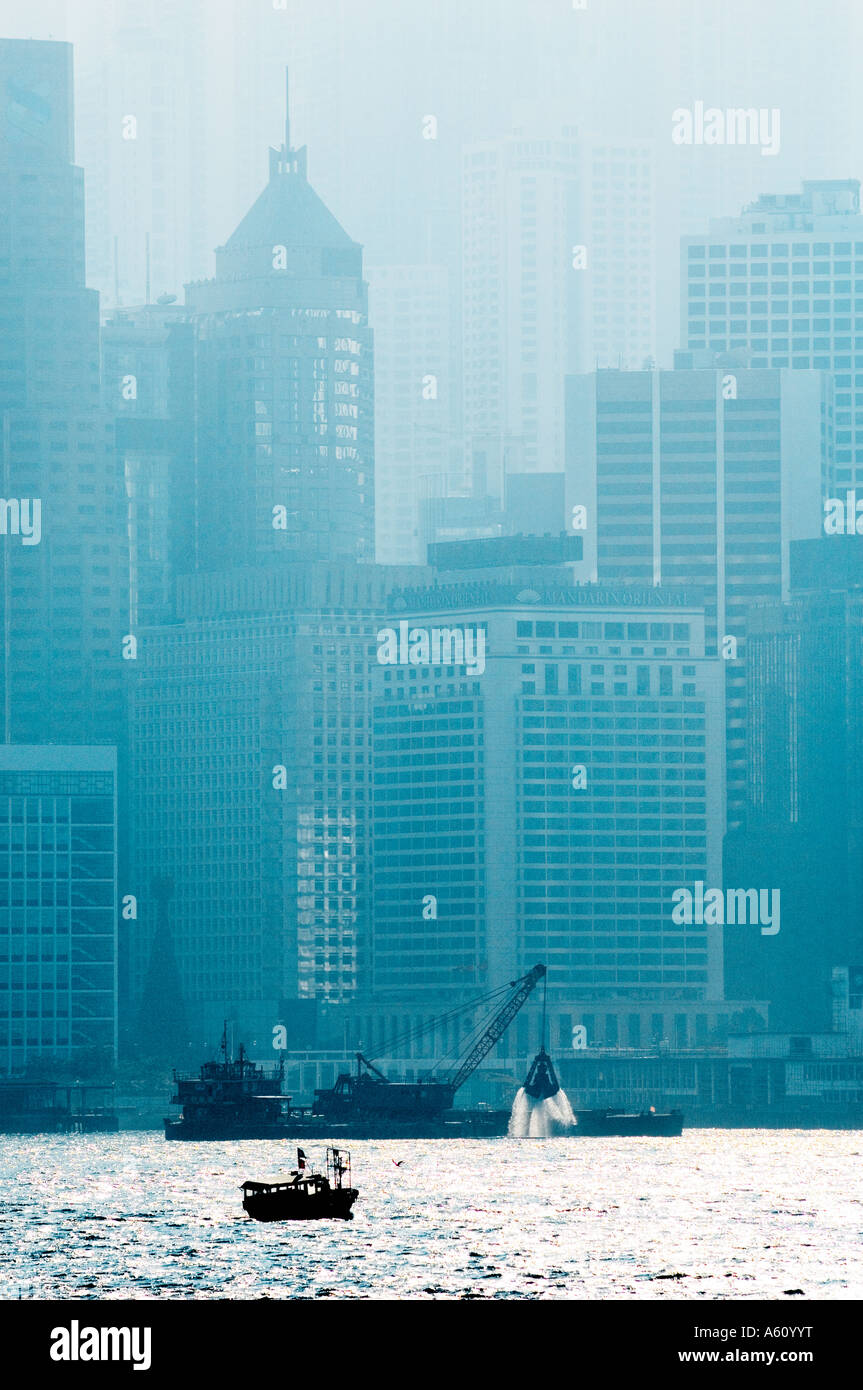 Draga barca limo di sollevamento dal Porto di Hong Kong Harbour con sfondo dell'Isola di Hong Kong per il distretto centrale alte torri Foto Stock