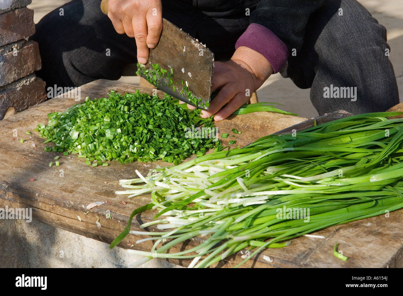 Rendendo tradizionale dim sum gnocchi Cinesi. Tritare le cipolle di primavera al di fuori agriturismo cucina. Provincia di Shandong, Cina Foto Stock