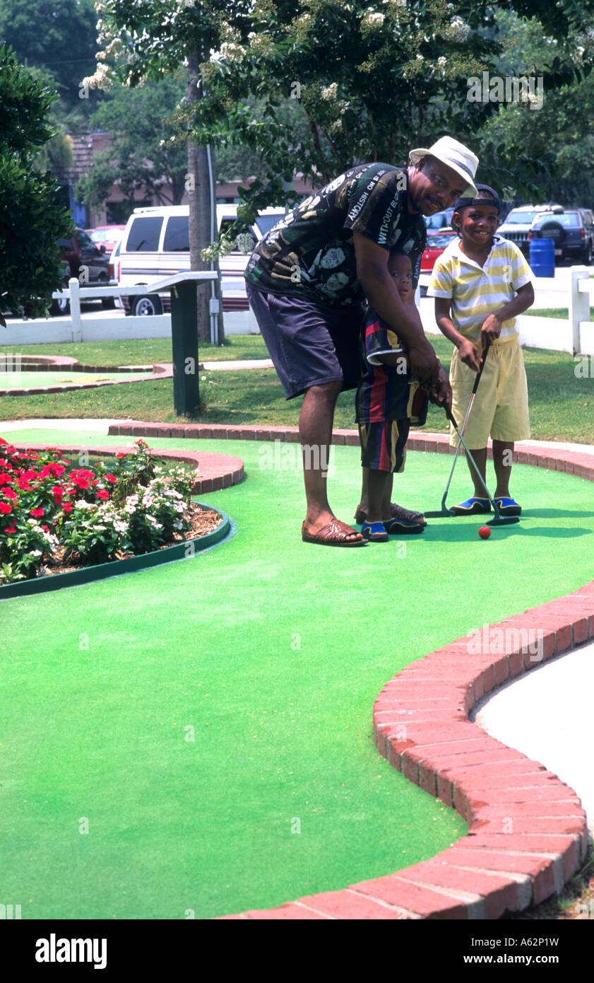 Balck African American uomo giocando a golf in miniatura con bambini piccoli Foto Stock