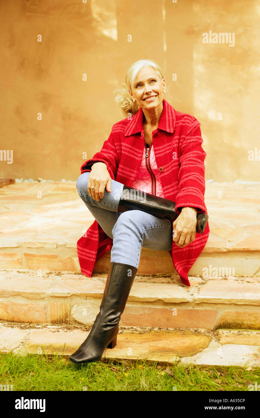 Senior donna seduta con le gambe incrociate al ginocchio e sorridente Foto Stock
