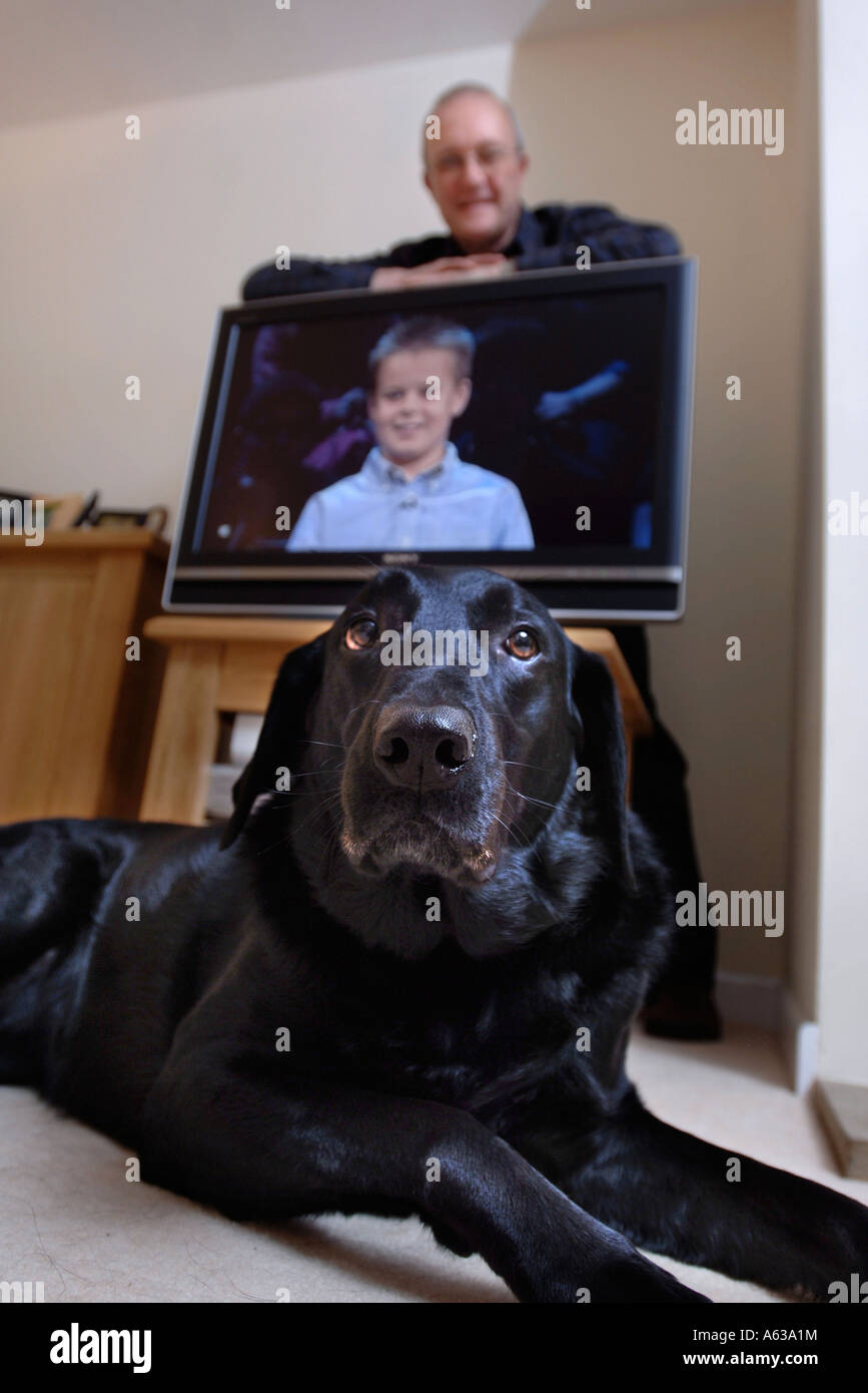 Un uomo di mezza età si appoggia su un televisore mentre un PET labrador nero giace sul piano REGNO UNITO Foto Stock