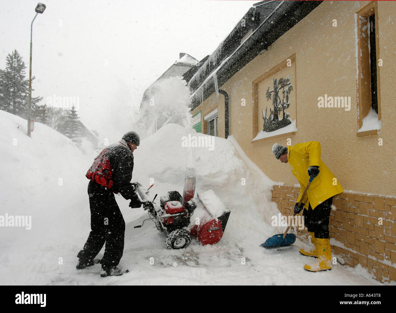 Gli uomini di spostare la neve in un appartamento casa utilizzando un sistema automatico di spalaneve a Oberwiesenthal, Monti Metalliferi, Erz Monti Metalliferi, Sassonia Foto Stock