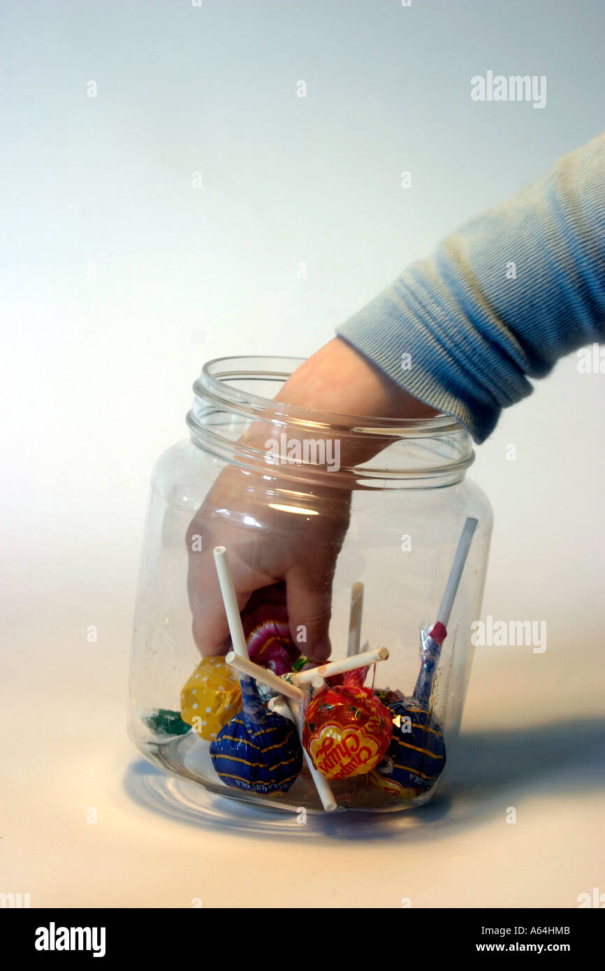 Una mano prendendo un lecca-lecca dolce da una selezione di lecca-lecca dolci in un vaso contro un blu e sfondo bianco Foto Stock