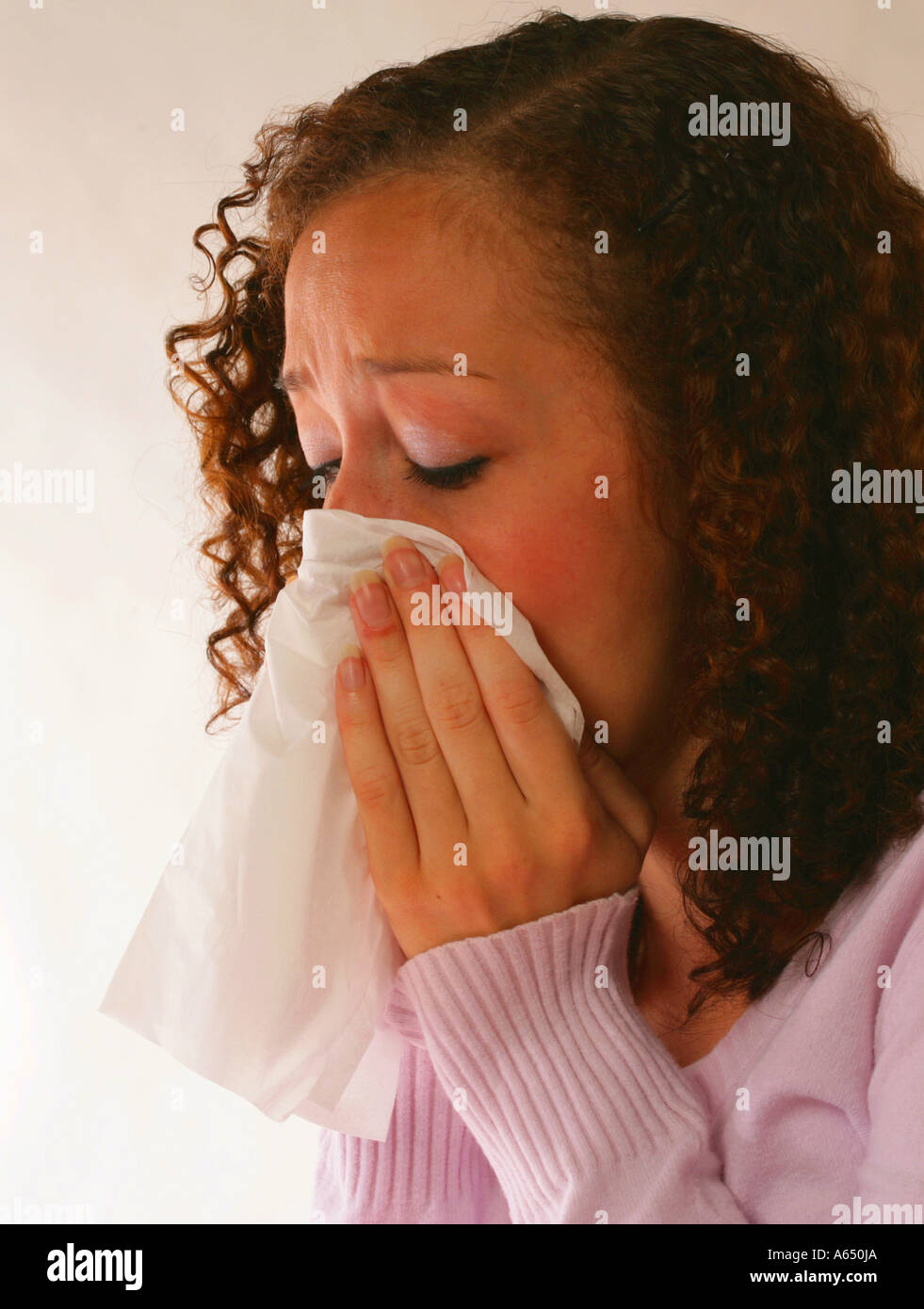 Giovane donna starnuti e soffiare il naso, utilizzando un tessuto. Essa può essere malati o soffre di allergie. Foto Stock