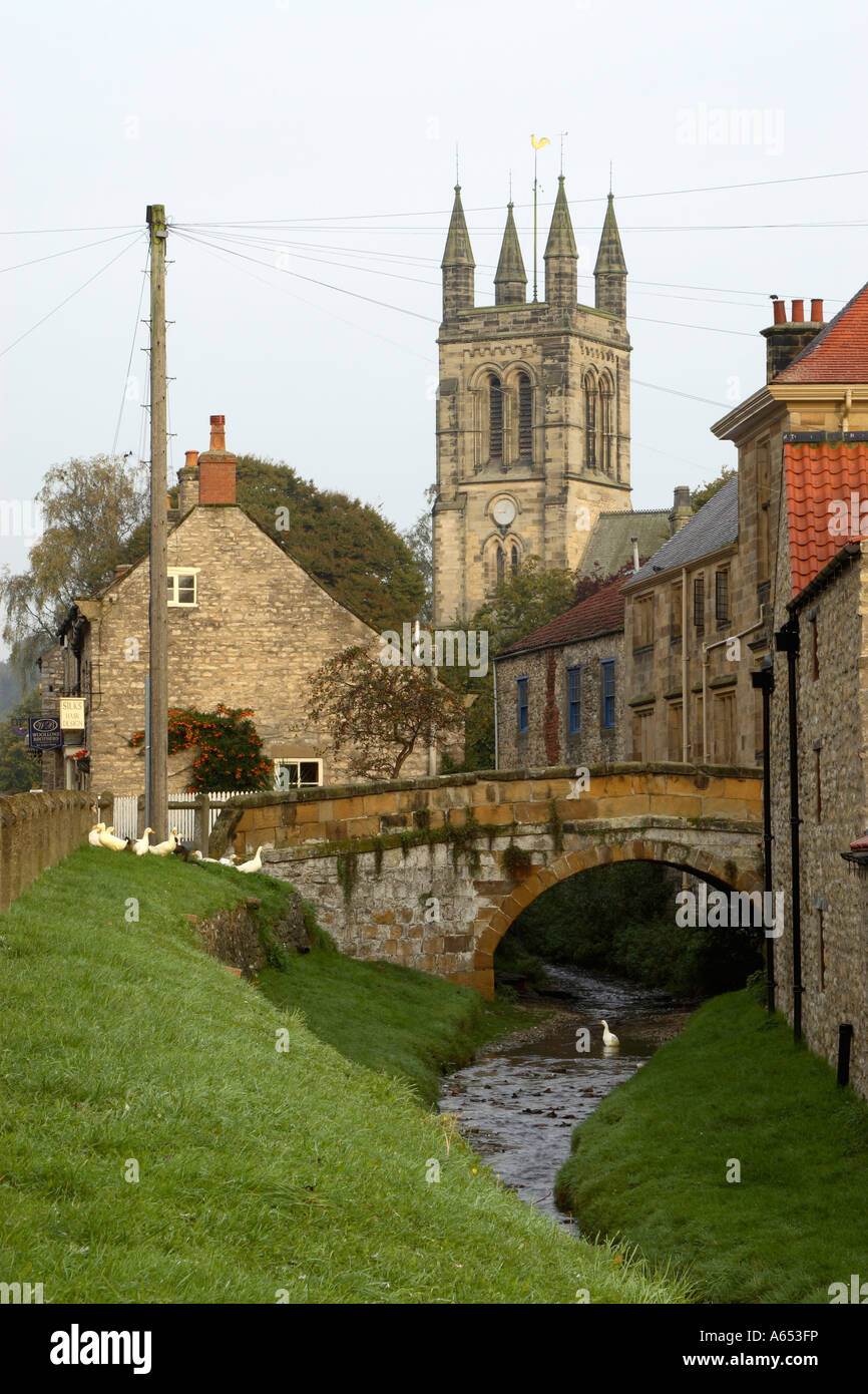 Il mercato vecchio villaggio di Helmsley che mostra la Chiesa opera in pietra birdge oltre Etton Beck e oche sulle banche erbosa Foto Stock