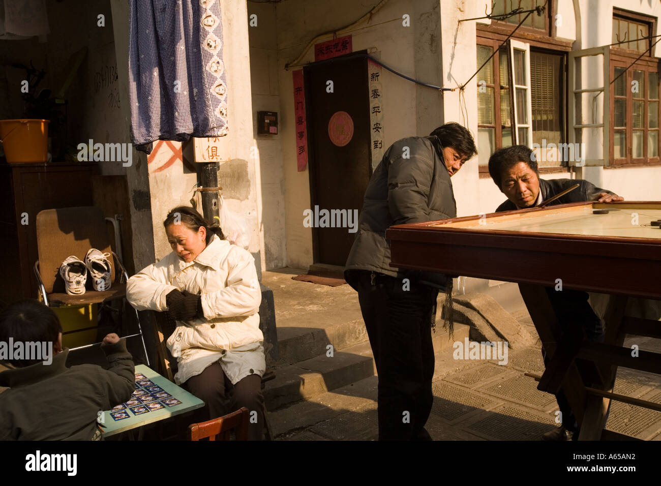 Gli uomini di giocare a biliardo in Zhoushan Lu in Hong kou mentre un bambino si siede e gioca un gioco da tavolo con sua madre, Shanghai, Cina Foto Stock