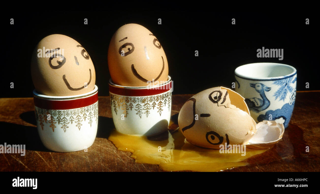 Tre uova in coppe d'uovo con i volti uno è caduto fuori Foto Stock