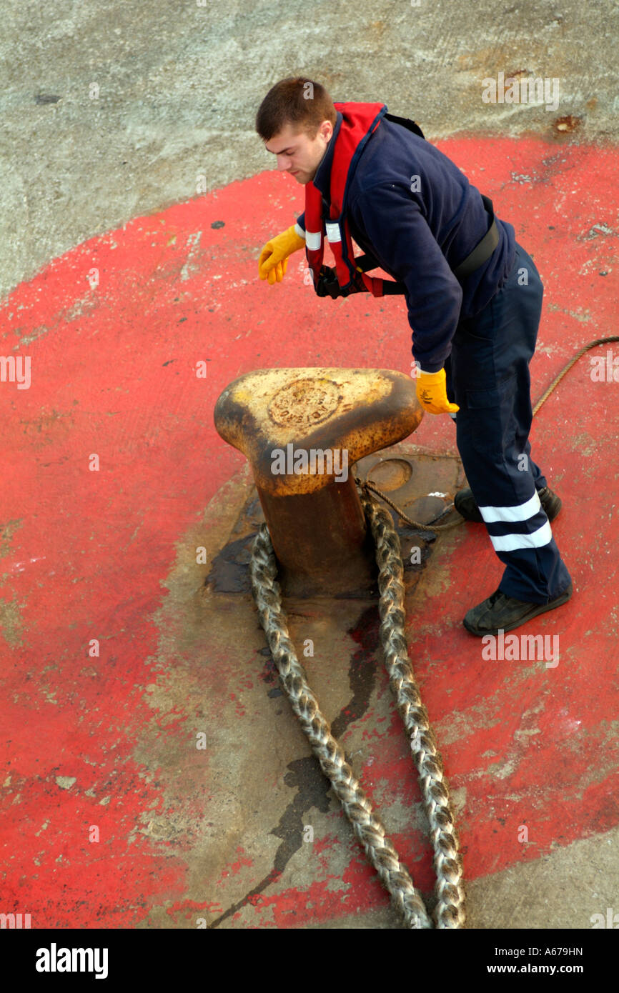 Membro di equipaggio giallo da indossare guanti di gomma rimuovendo una delle navi la cima di ormeggio dalla banchina Foto Stock