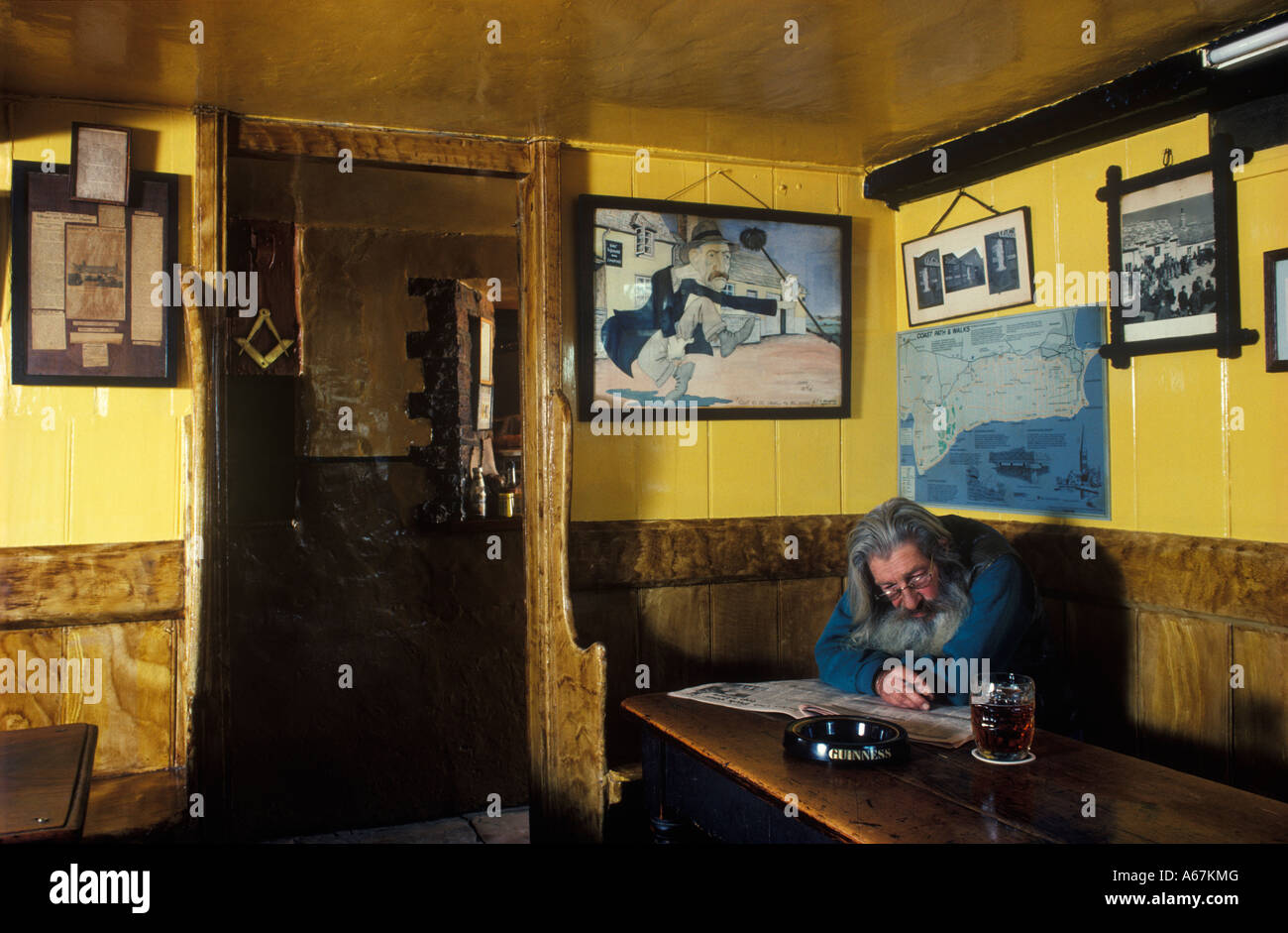 Pub Square e Compass, Ray Newman publican. Worth Matravers, Dorset. Fumare leggendo una pinta di birra di giornale sotto un ritratto di suo padre Charlie. Foto Stock