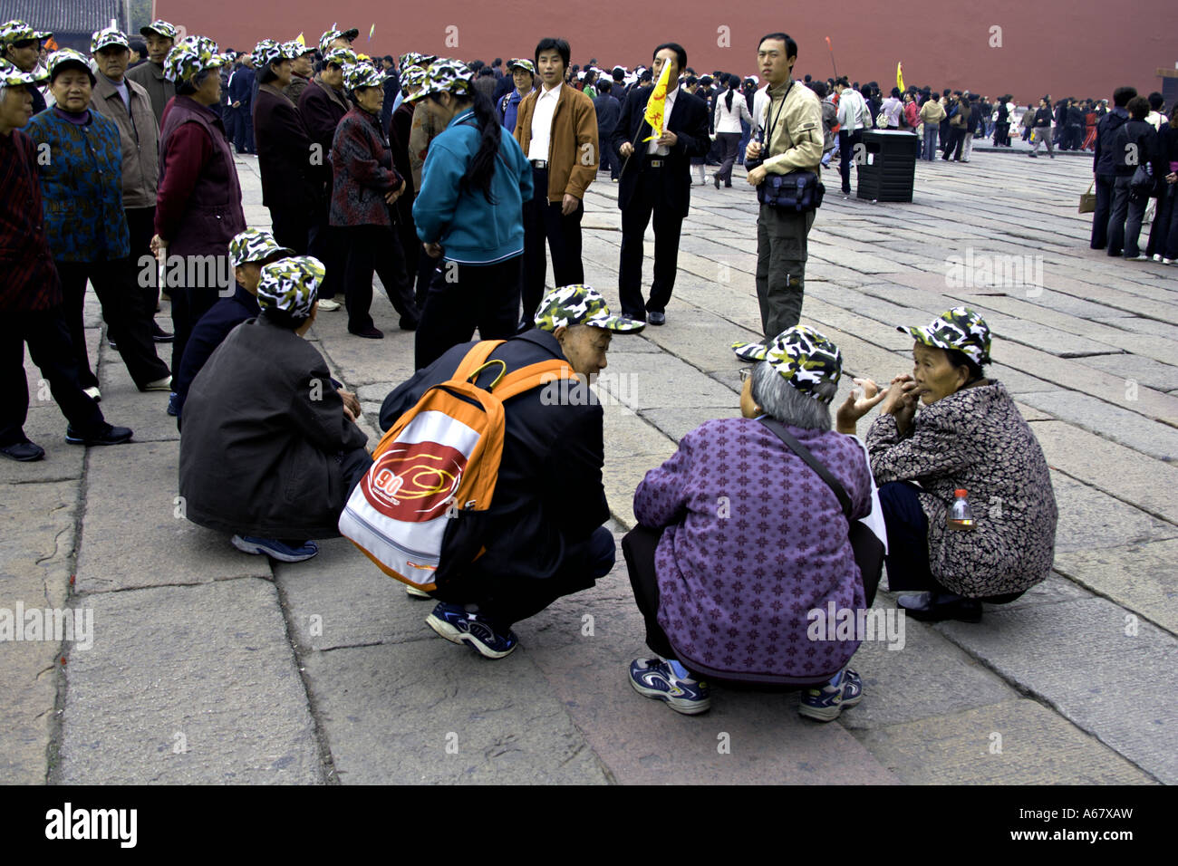 Cina Pechino tour cinese gruppo camuffamento Indossando cappellini da baseball squat insieme in attesa di accedere alla Città Proibita Foto Stock