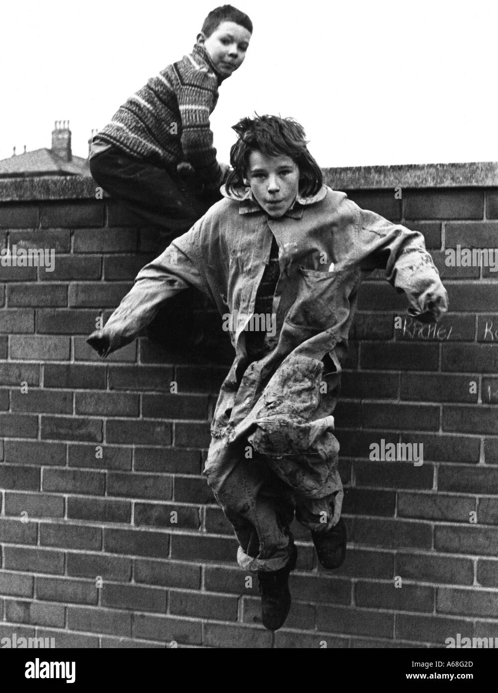 Giovani ragazzi fuori scuola saltando oltre il muro anni '70 Foto Stock