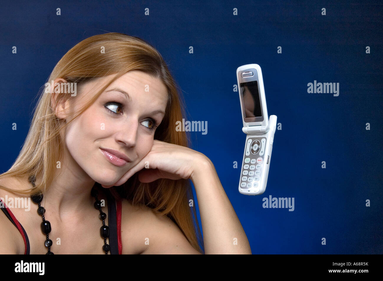 Giovane donna bionda guardando un Motorola Razr cellulare che aleggia nell'aria. Girato su sfondo blu Foto Stock