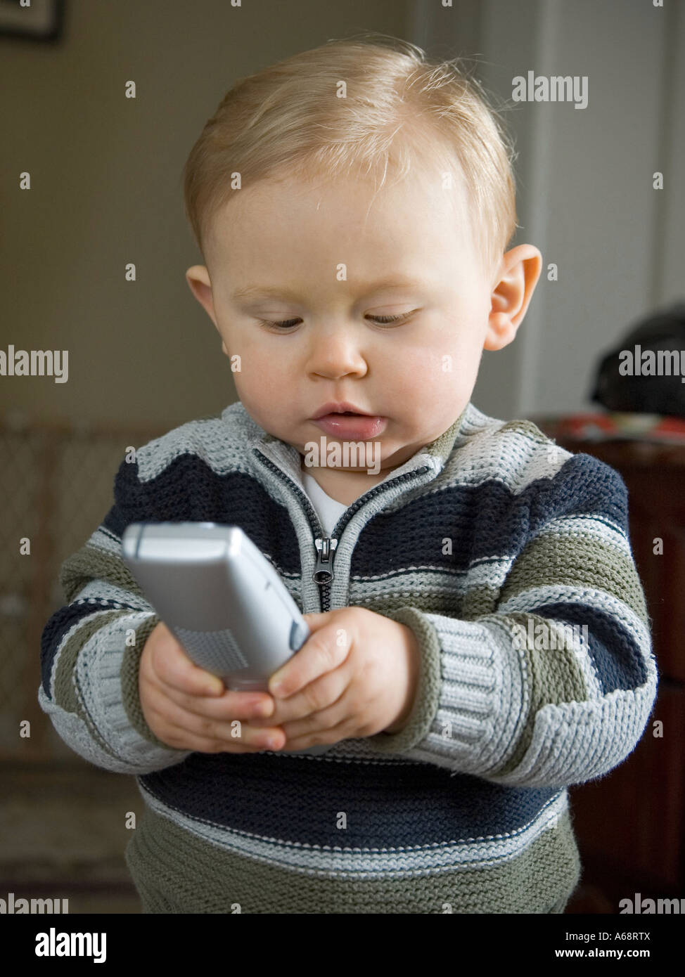 Un anno di età baby boy in un maglione alla ricerca di un telefono wireless ricevitore Foto Stock