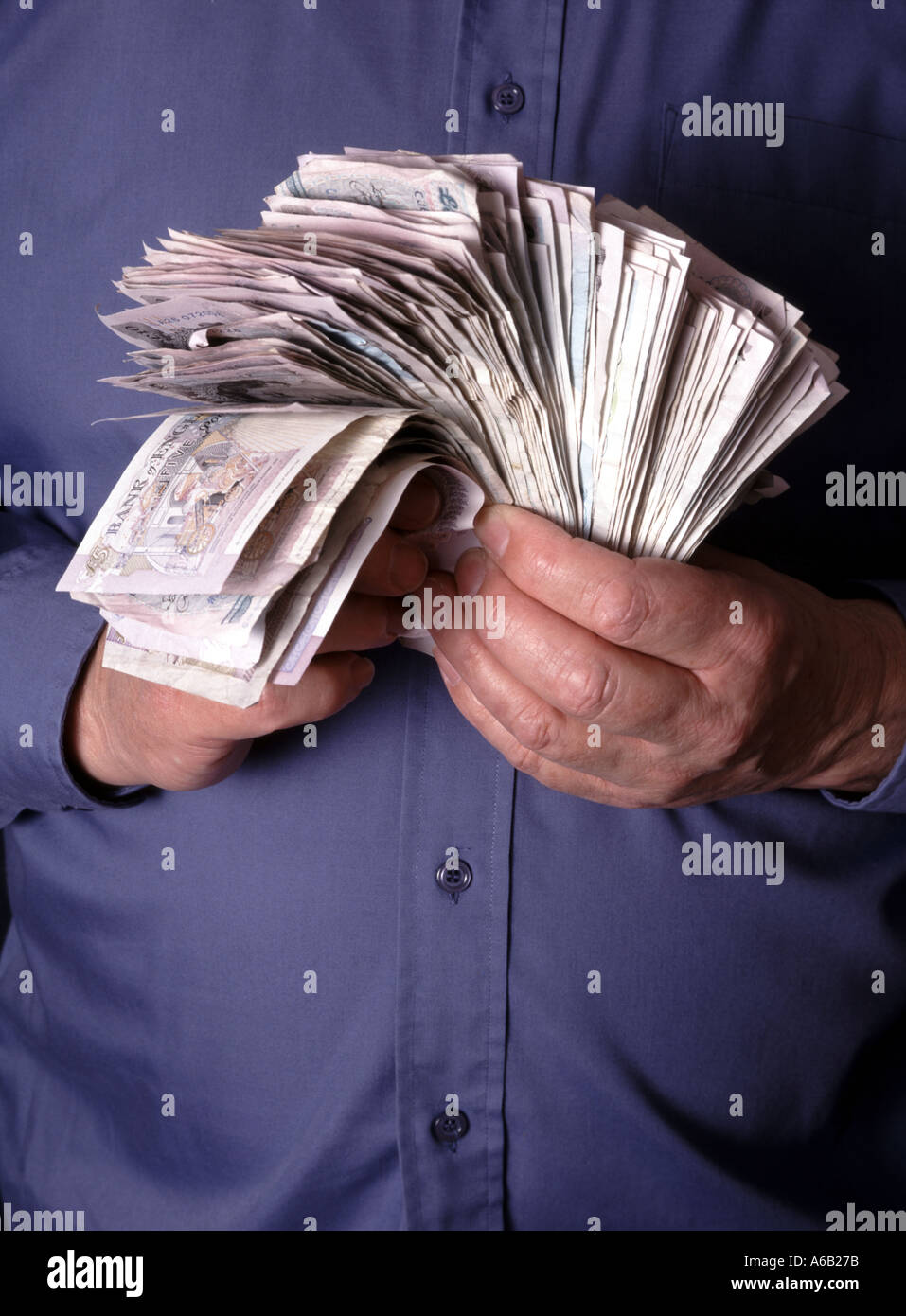 Un uomo d'affari stringe due mani e tiene in mano pile di contanti assortiti in banconote da sterlina prodotte dal modello England UK Foto Stock