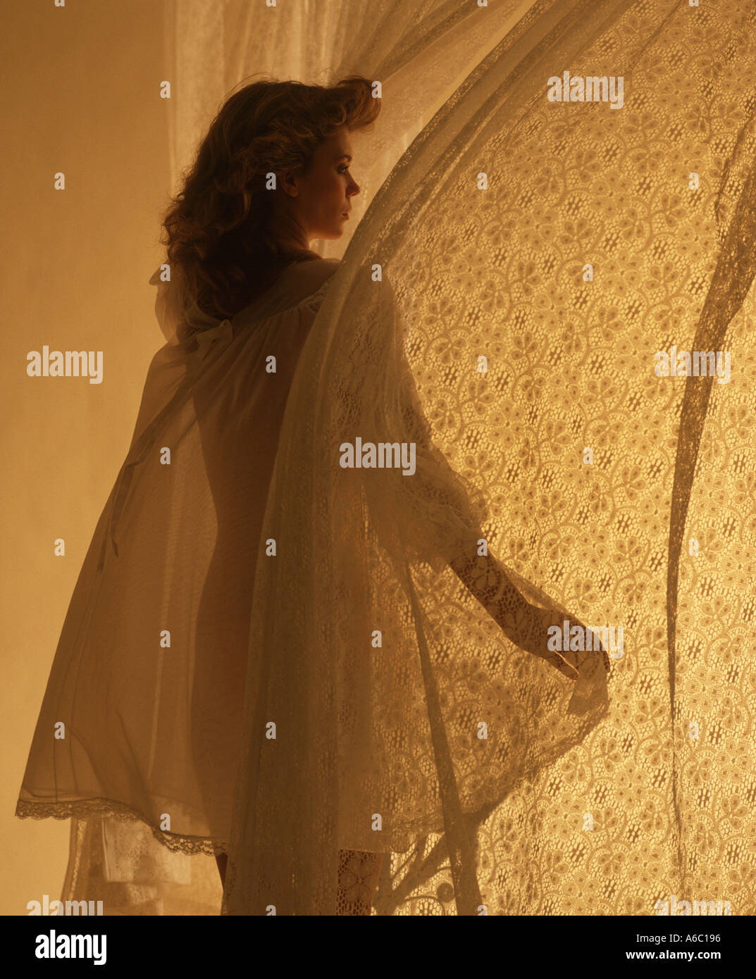 Donna in nightgown guardando fuori camera da letto finestra ventoso Foto Stock