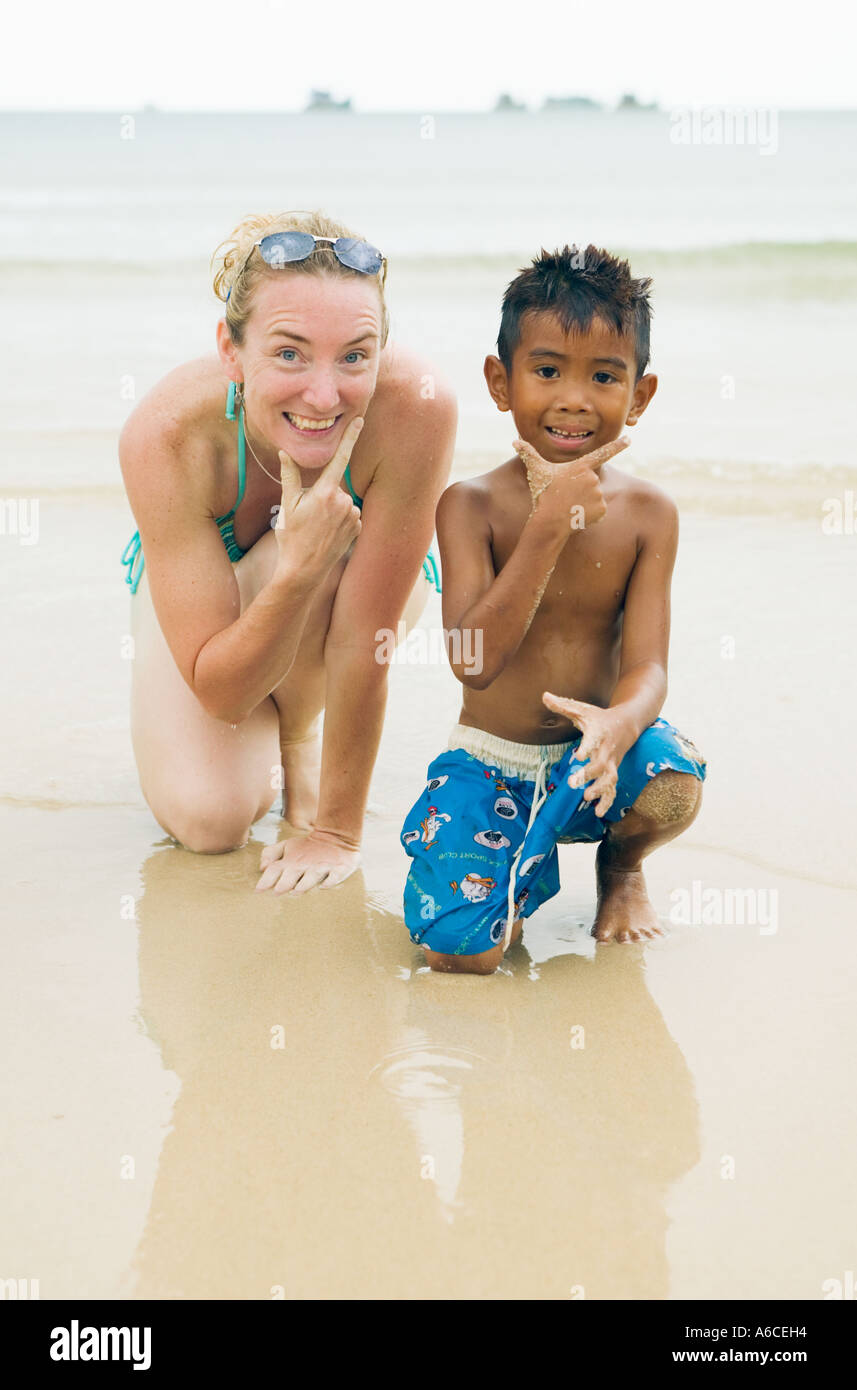 Metà 30s donna accovacciata su una spiaggia con un ragazzo thailandese Ko Phangnan Koh Phangan Thailandia Foto Stock
