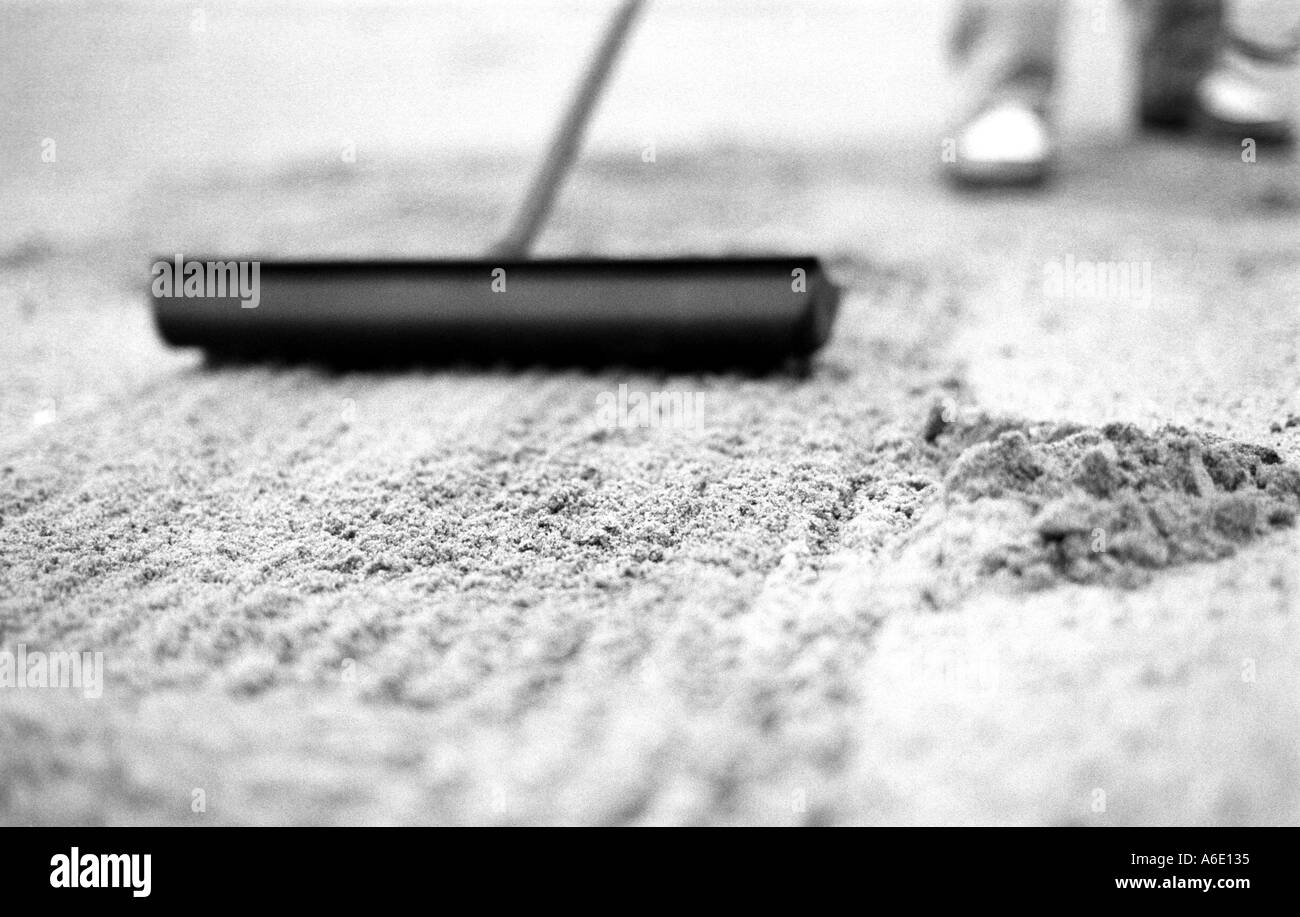 Un giocatore di golf a rastrellare una trappola sul corso. Foto Stock