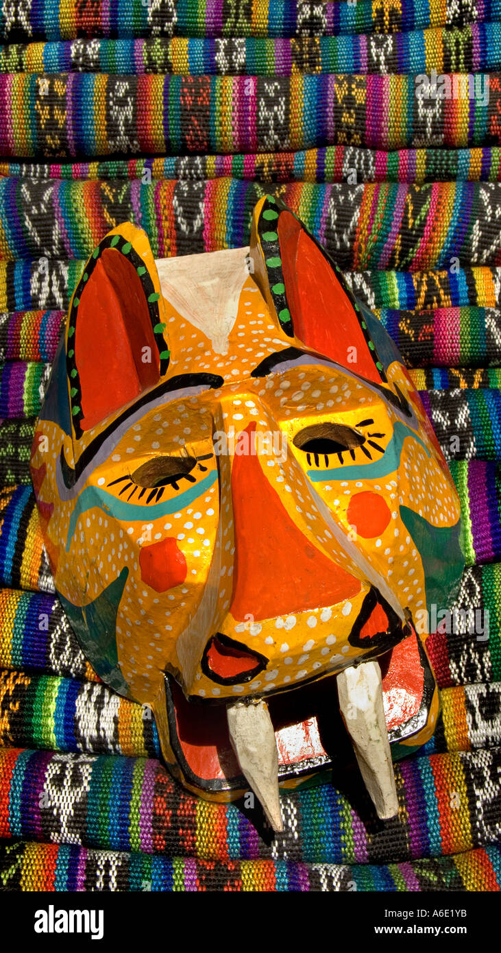 Guatemala danza in legno maschera di una Jaguar contro una pila di tessuti multicolore mercato Chichicastenango Guatemala Foto Stock