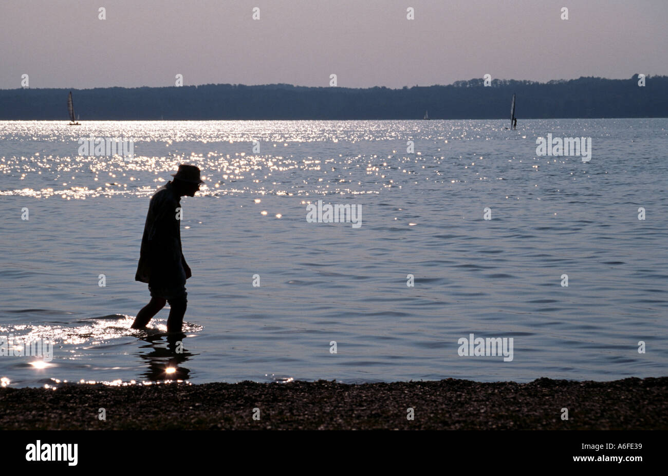 Un solitario vecchio uomo gode di una passeggiata in riva al lago di acqua in Baviera Germania Foto Stock