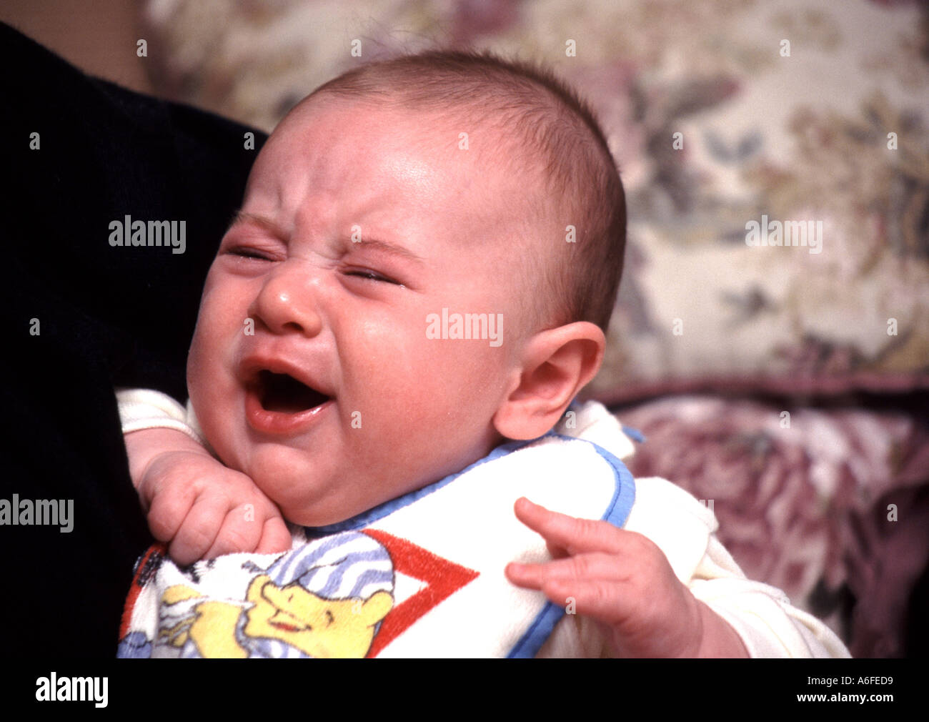 Ritratto di bambino 1996 primo piano che indossa un bavaglino che piange di rosso in faccia19 settimana modello rilasciato bambino tenuto dalla madre 1990s Essex Inghilterra Regno Unito Foto Stock