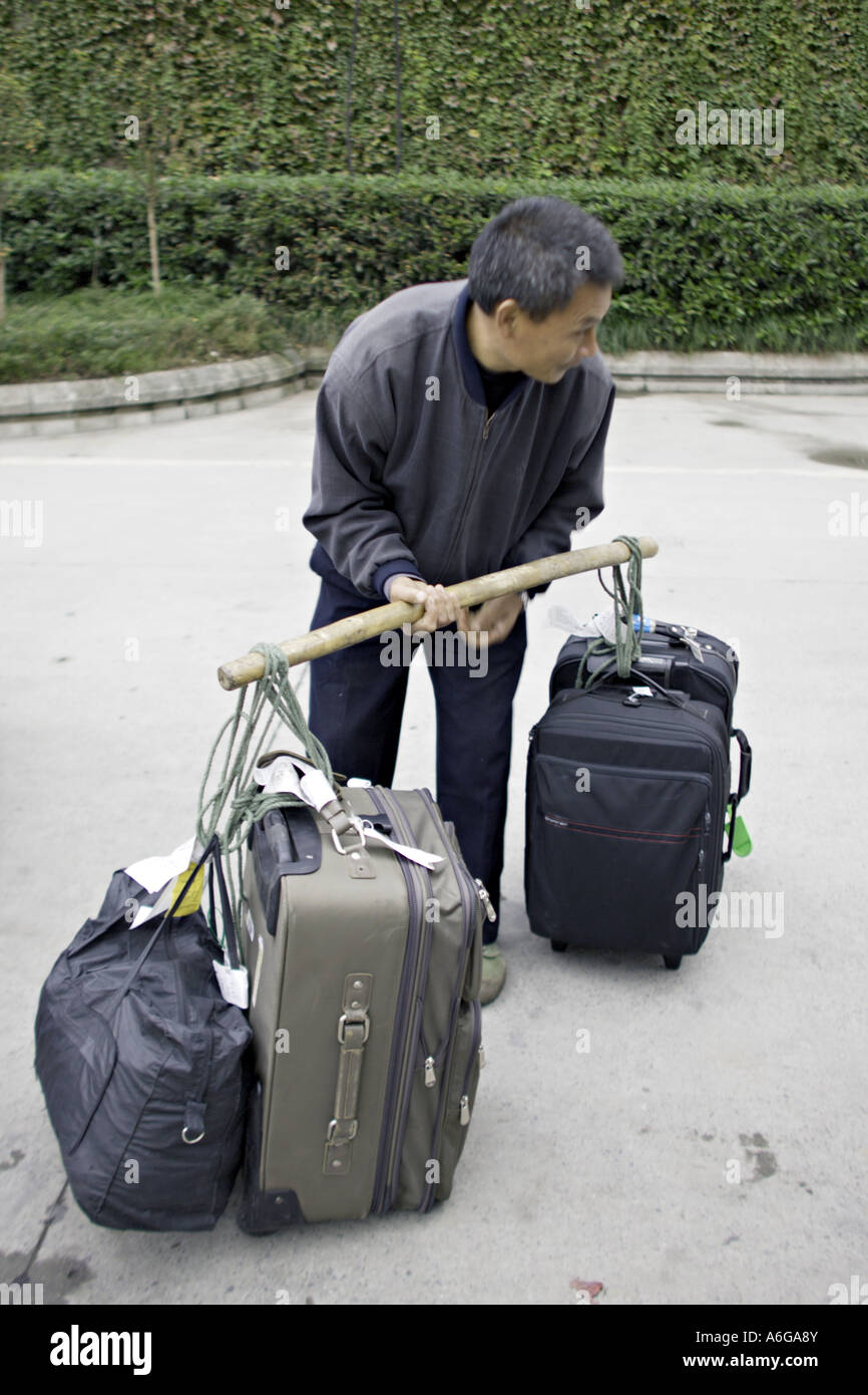 Cina CHONGQUING cinese del gestore per i bagagli si prepara a sollevare diverse valigie pesanti utilizzando un polo di spallamento Foto Stock