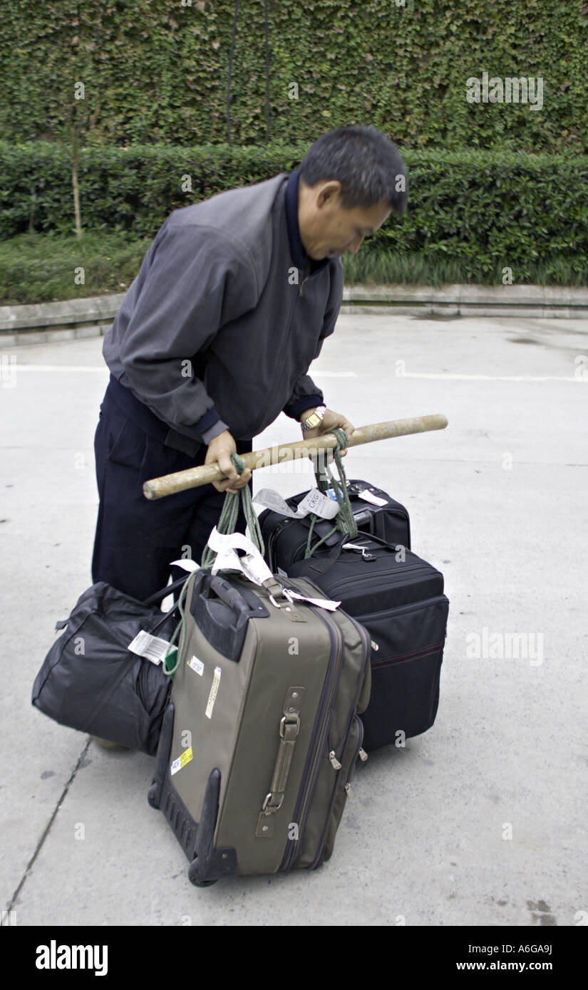 Cina CHONGQUING cinese del gestore per i bagagli si prepara a sollevare diverse valigie pesanti utilizzando un polo di spallamento Foto Stock