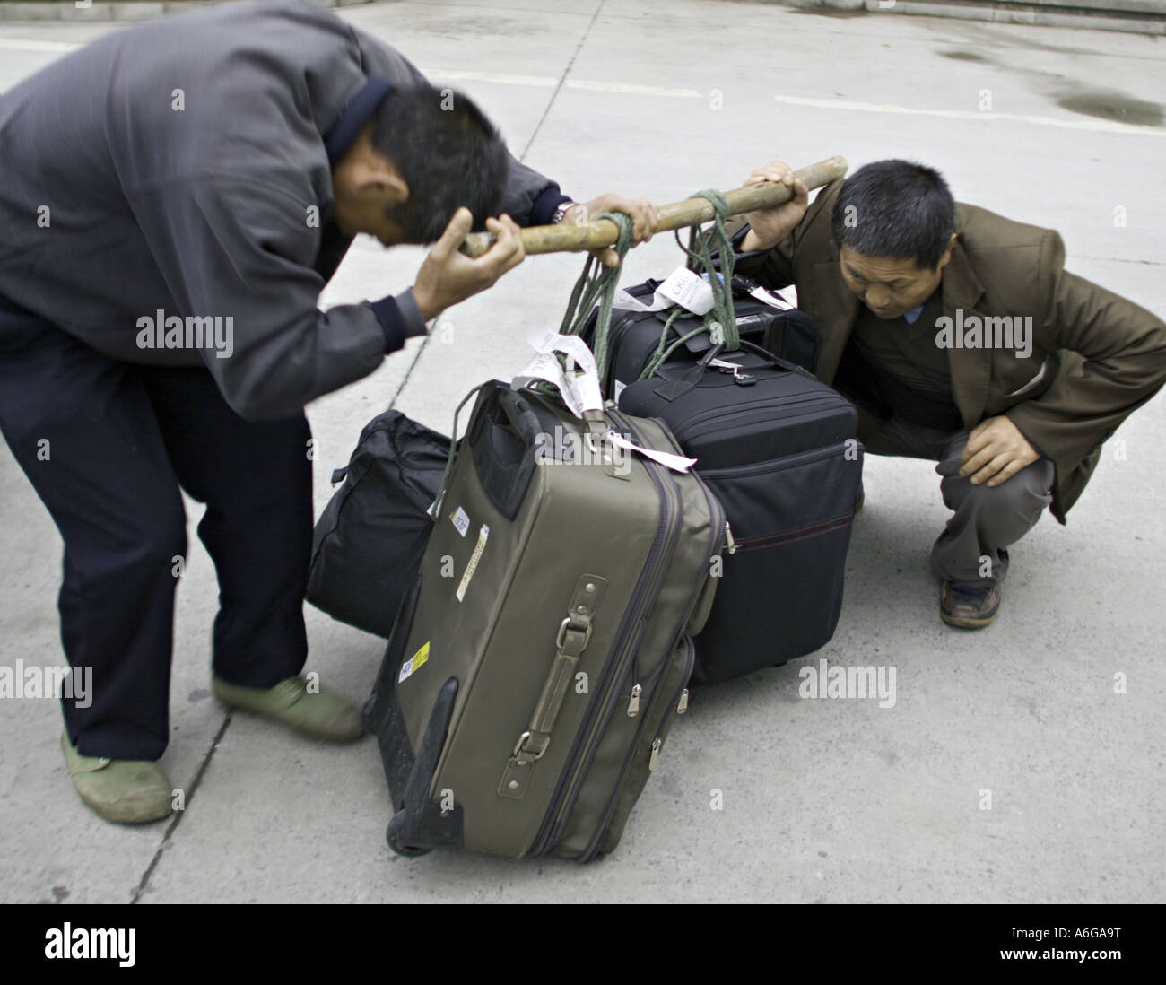 Cina CHONGQUING cinese di gestori di bagagli il ceppo di sollevare diverse valigie pesanti utilizzando un polo di spallamento Foto Stock