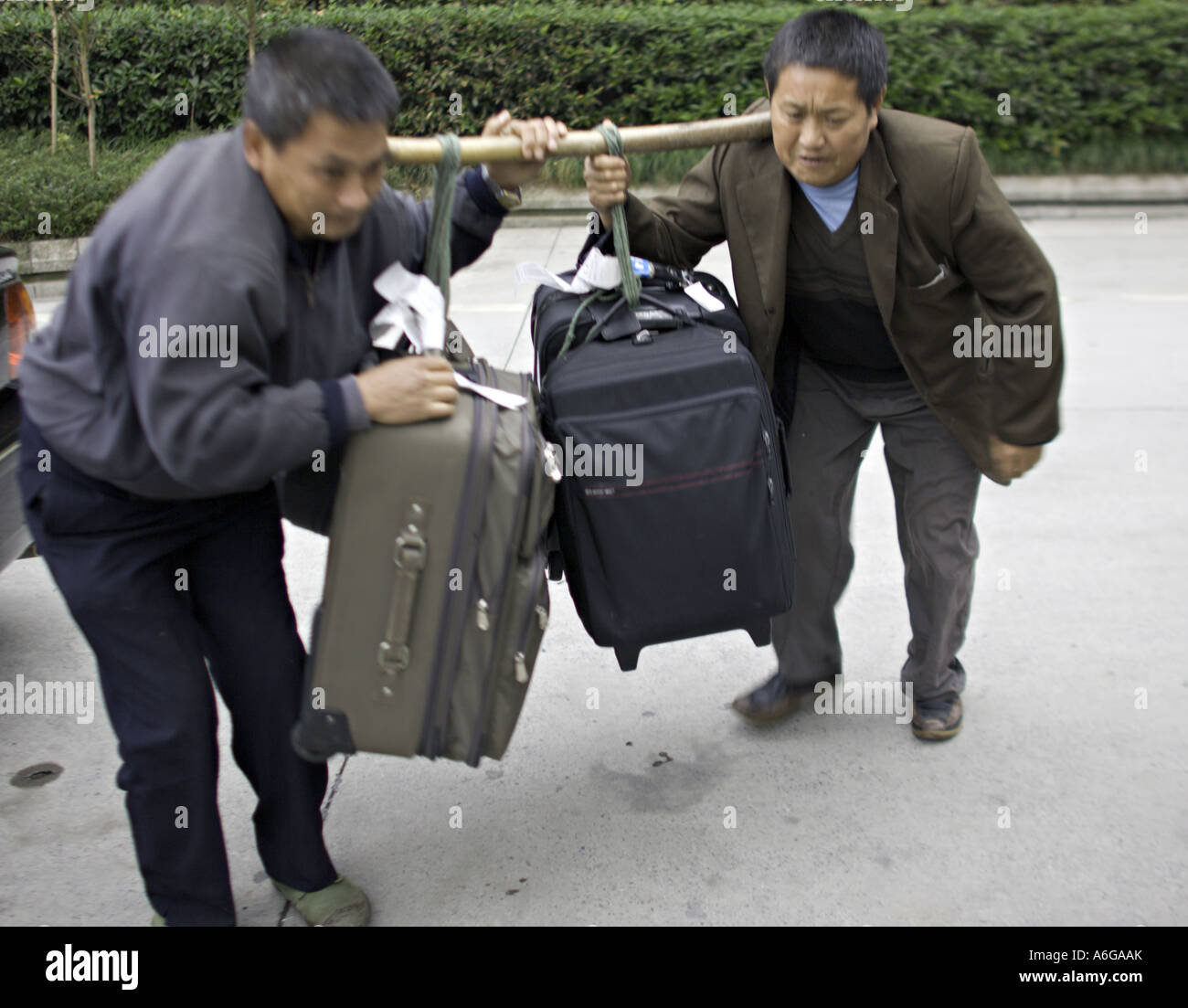 Cina CHONGQUING cinese di gestori di bagagli il ceppo di sollevare diverse valigie pesanti utilizzando un polo di spallamento Foto Stock