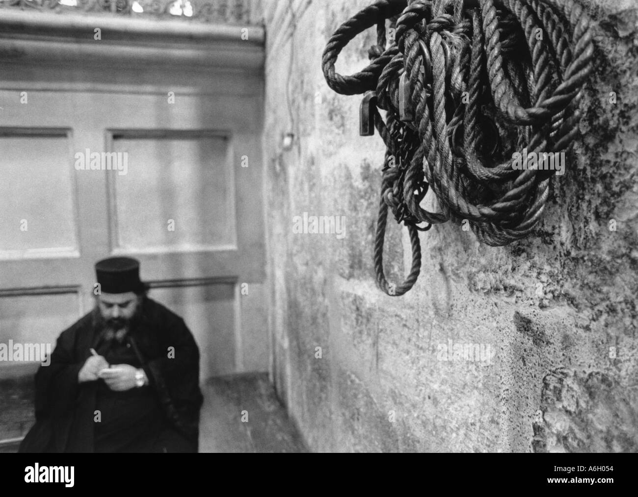Greco-ortodossi sacerdote seduto e la scrittura di campana unta corda nella chiesa del Santo Sepolcro di Gerusalemme la città vecchia Foto Stock