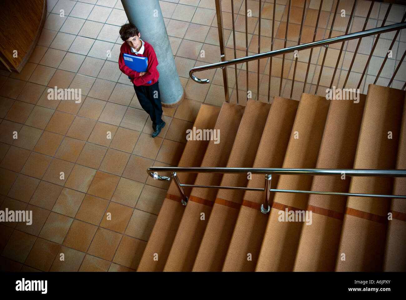 Junior scolaro con cartella in aula in attesa solo nella tromba delle scale della scuola Foto Stock