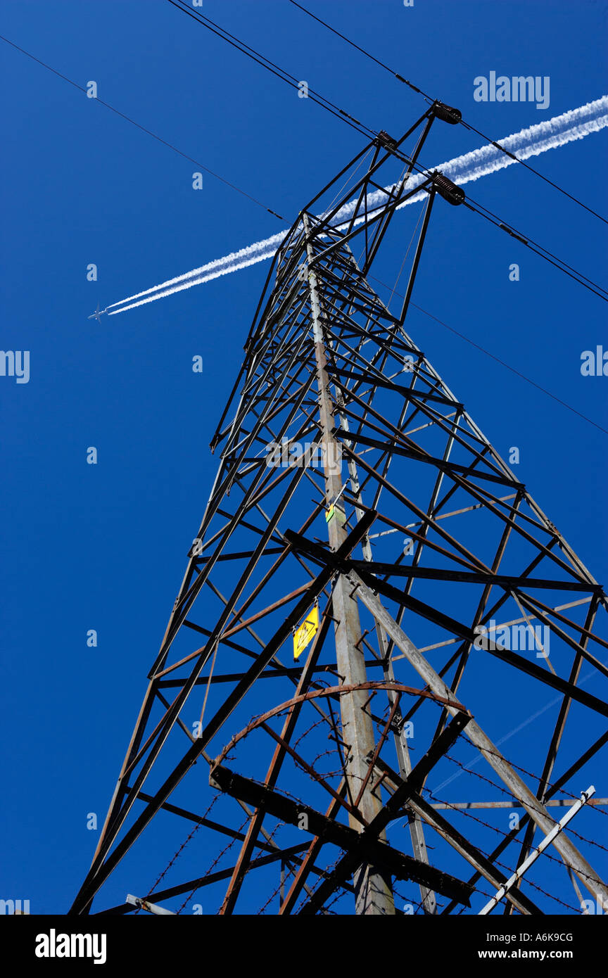 Pilone di elettricità e i cavi con il percorso di scarico dei velivoli a getto nel cielo blu Foto Stock
