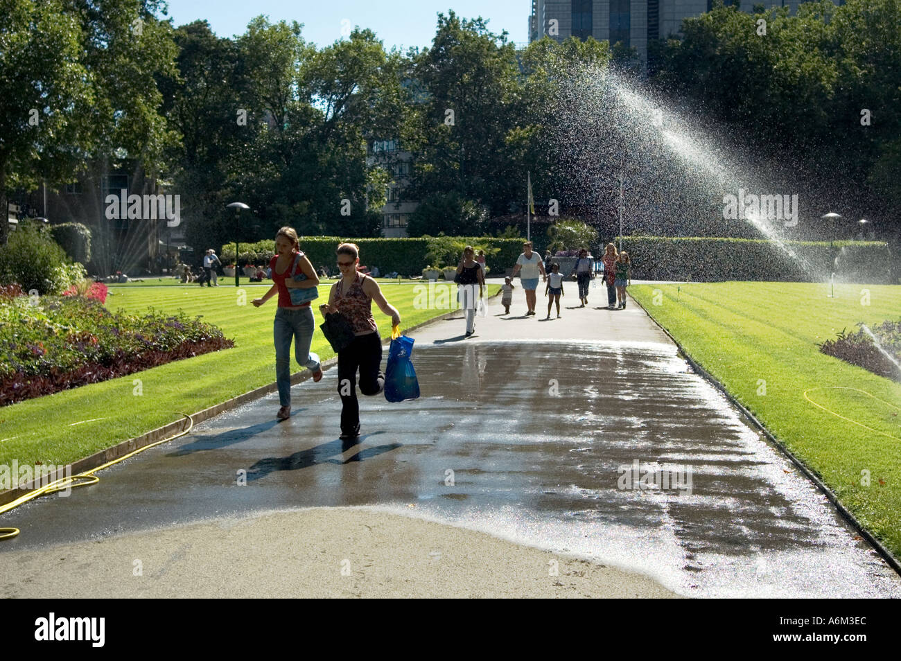 Ragazze schivare gli sprinkler acqua durante una ondata di caldo Victoria Embankment Gardens Londra Centrale Foto Stock