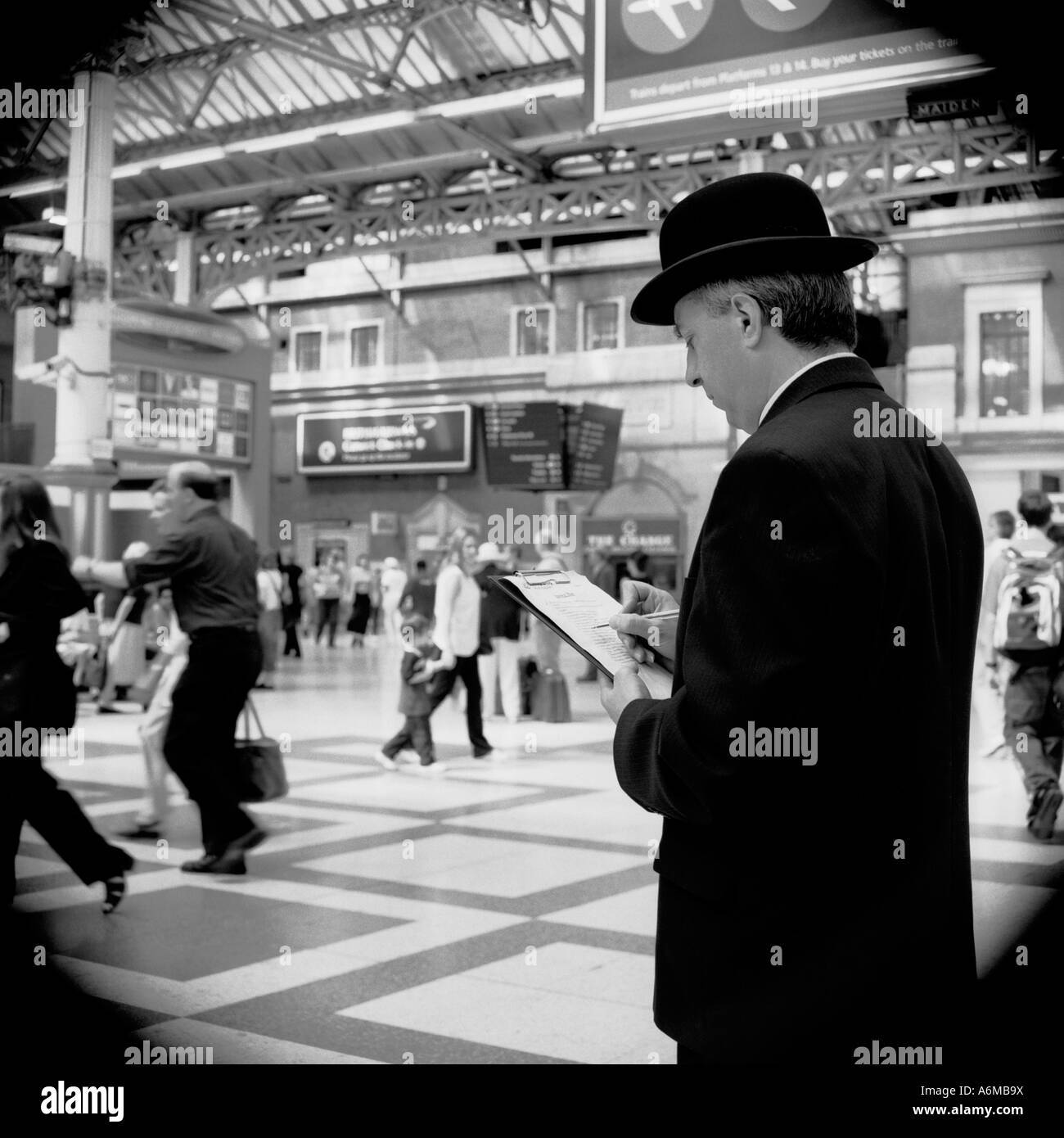 Uomo con appunti alla stazione ferroviaria prendendo appunti. Cappello e vestito City gent che fanno ricerca Foto Stock