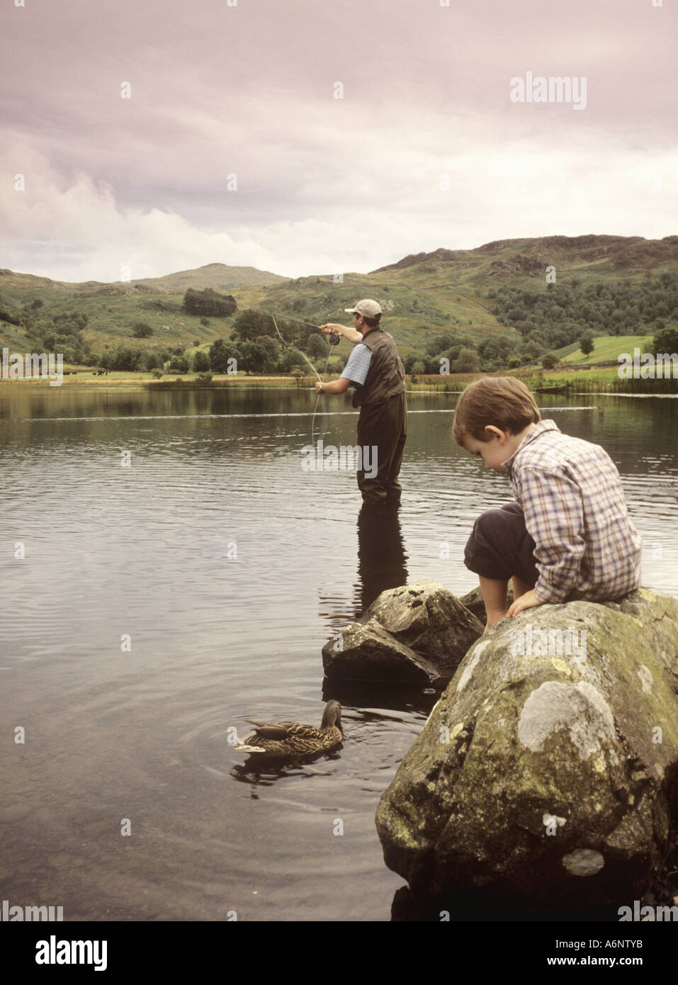 Padre dimostrando "fly fishing' a suo figlio a Watendlath Tarn, Cumbria, Lake District, England, Regno Unito Foto Stock