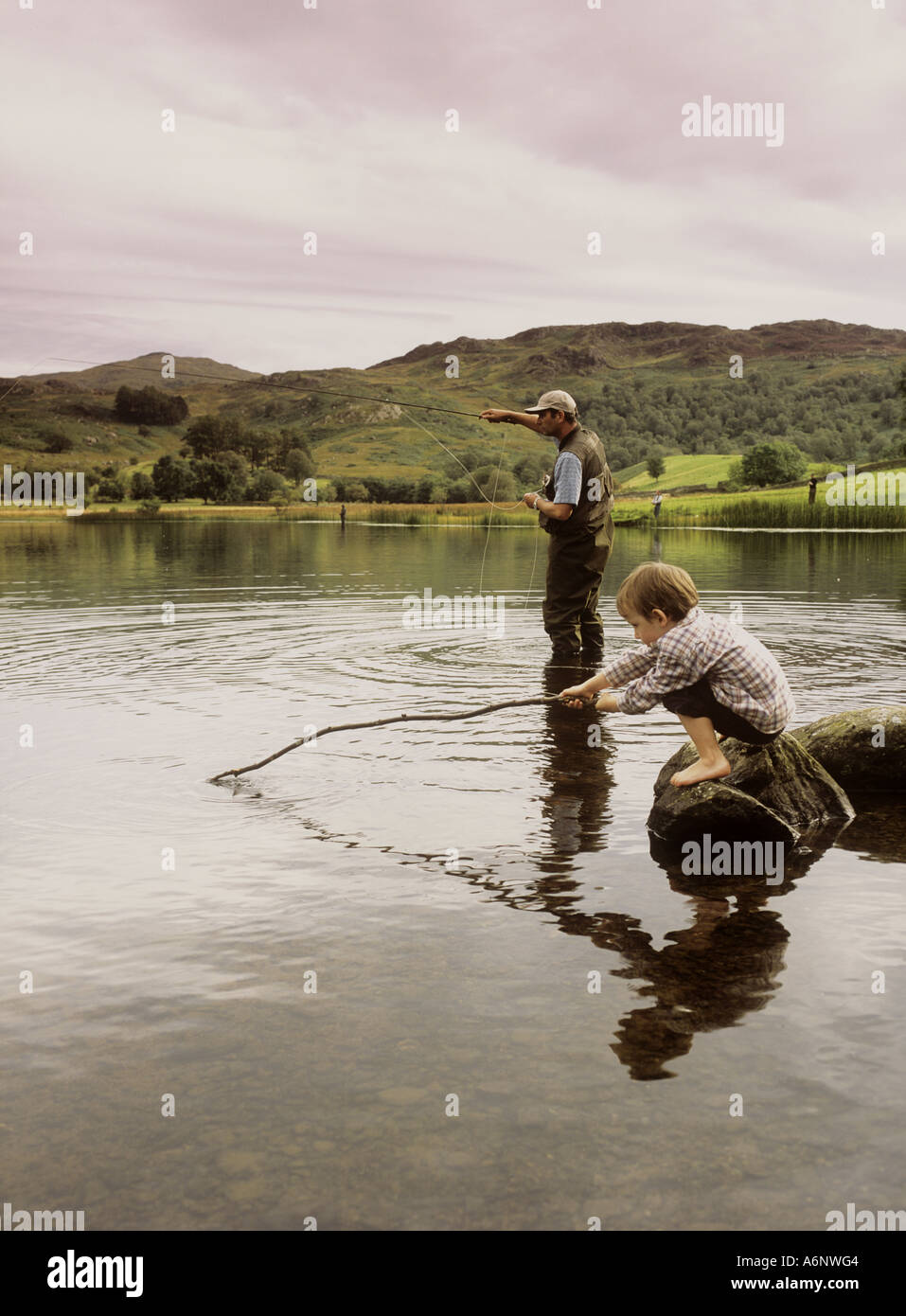 Padre dimostrando "fly fishing' a suo figlio a Watendlath Tarn, Cumbria, Lake District, England, Regno Unito Foto Stock