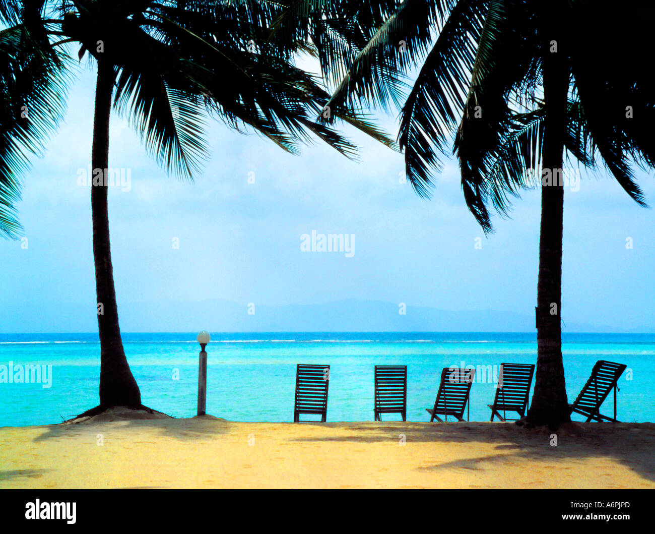 Cielo azzurro e limpido mare con vista attraverso le palme e la linea di sedie a sdraio sulla spiaggia IN THAILANDIA Foto Stock