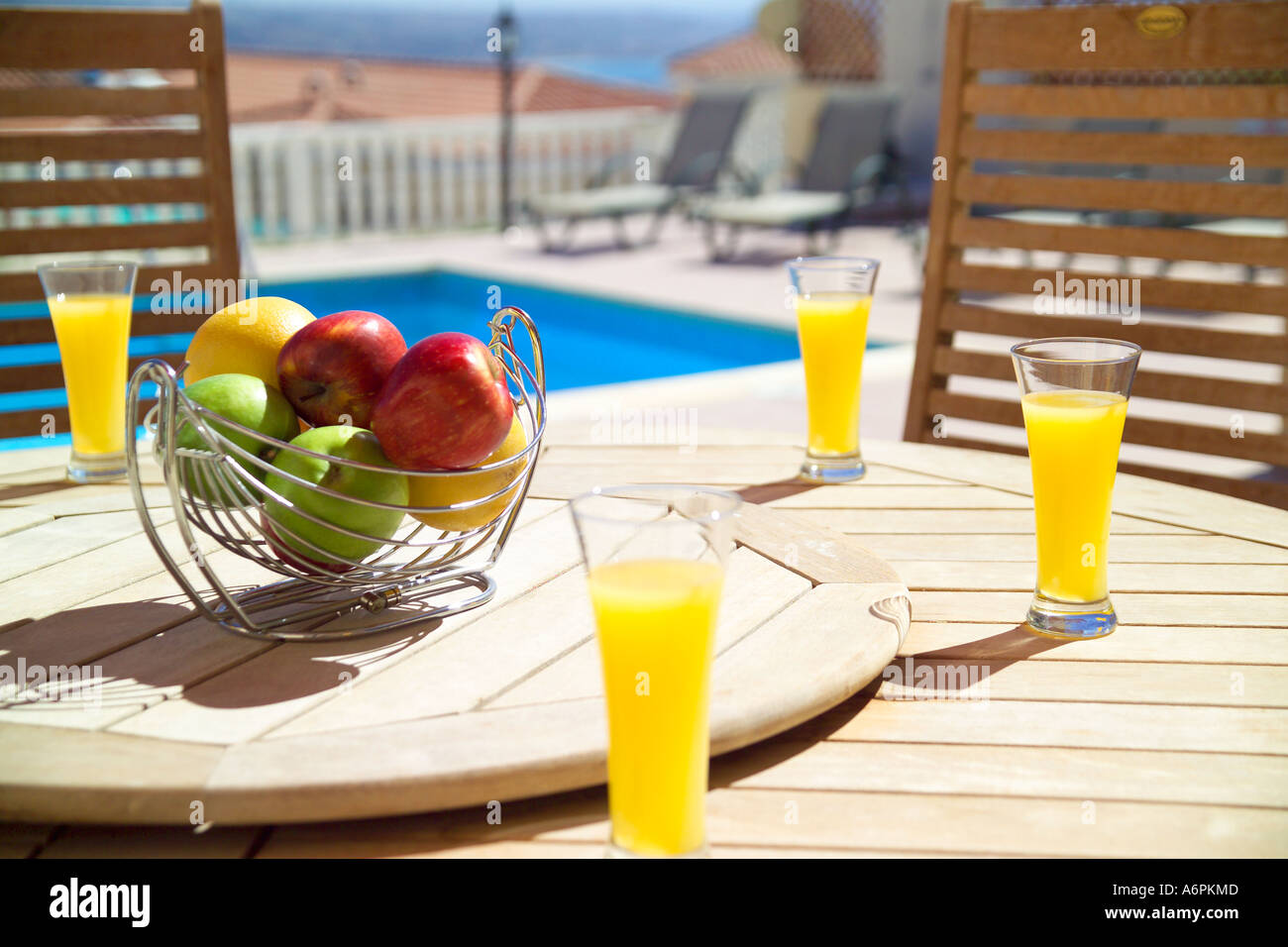 Ciotola di frutta e bicchieri di succo di arancia sul tavolo di legno CON PISCINA IN BACKGROUND IN CIPRO Foto Stock
