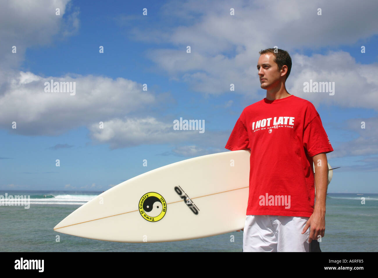 Uomo in rosso tshirt tenendo la tavola da surf con poco nuvoloso cielo e oceano onde in background Honolulu Oahu Hawaii Foto Stock