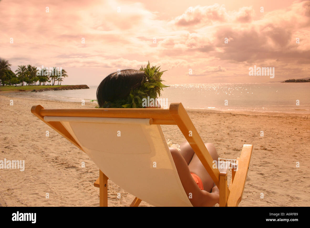 Donna in reclinabile sedia spiaggia indossando haku lei guardando il tramonto sulla spiaggia di sabbia di Oahu Hawaii Foto Stock