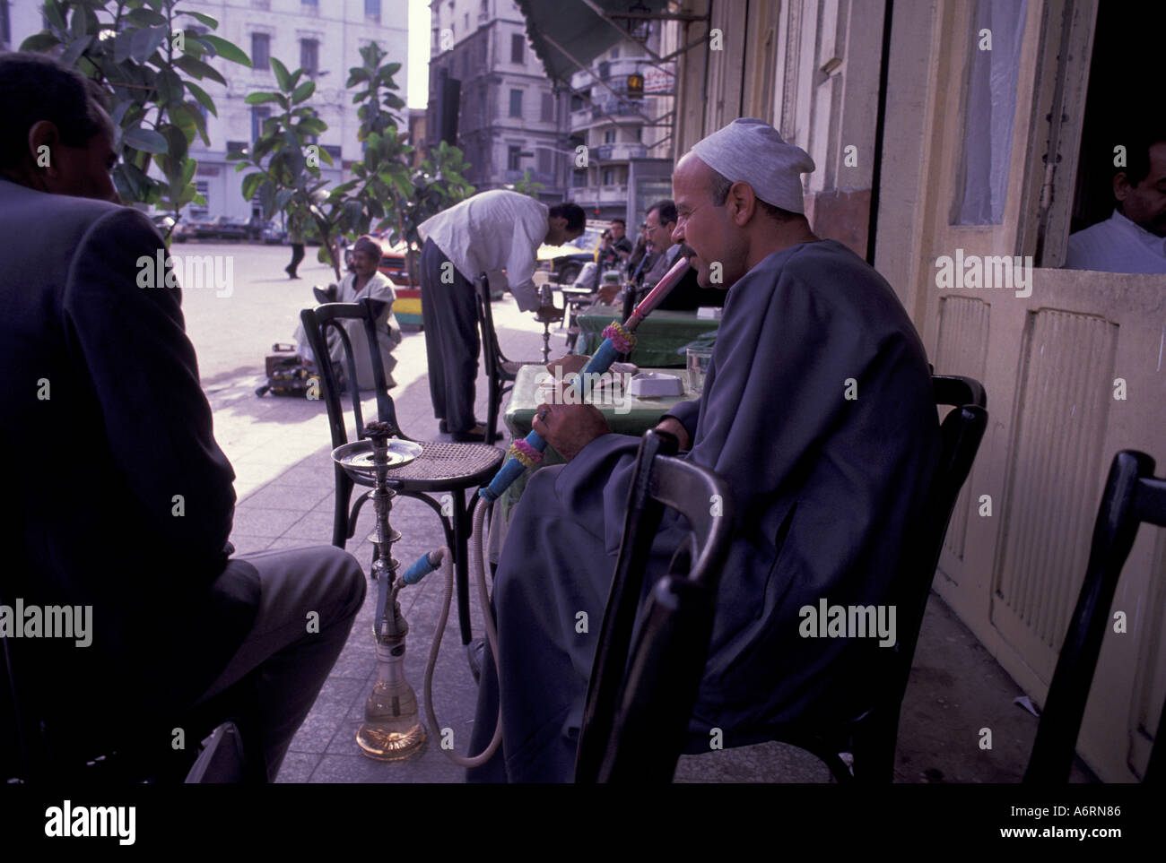 Africa, Egitto, Alessandria. Uomo di fumare in un cafè sul marciapiede Foto Stock