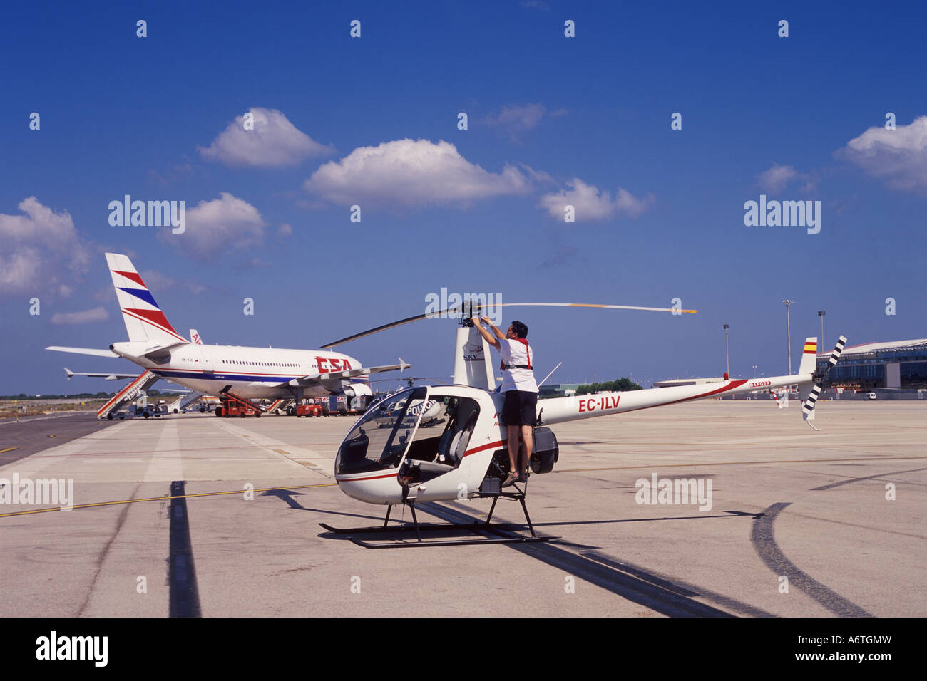 Pilota, indossare il giubbotto di salvataggio, che esegue il pre-volo controlli su Robinson R22 elicottero + CSA aereo di linea a Mahon, Aeroporto Menorca Foto Stock