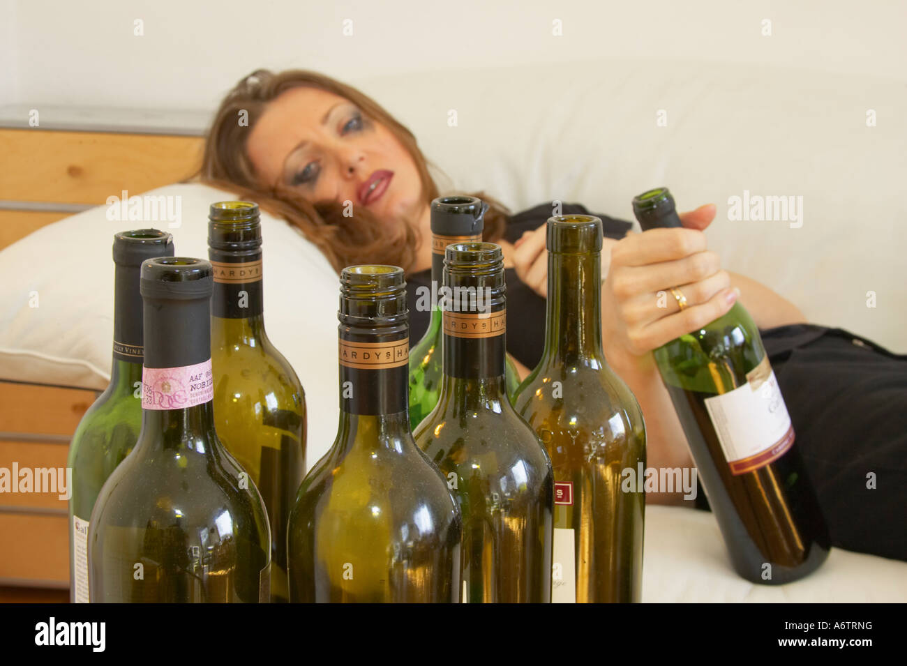 Giovane donna disteso sul lettino tenendo la bottiglia di vino dopo aver bevuto troppo Foto Stock