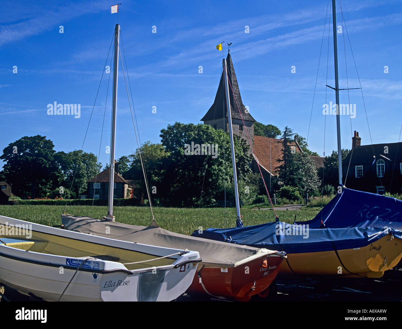 BOSHAM WEST SUSSEX REGNO UNITO Giugno guardando attraverso il villaggio verde verso la Chiesa della Santa Trinità con spiaggiata barche in primo piano Foto Stock