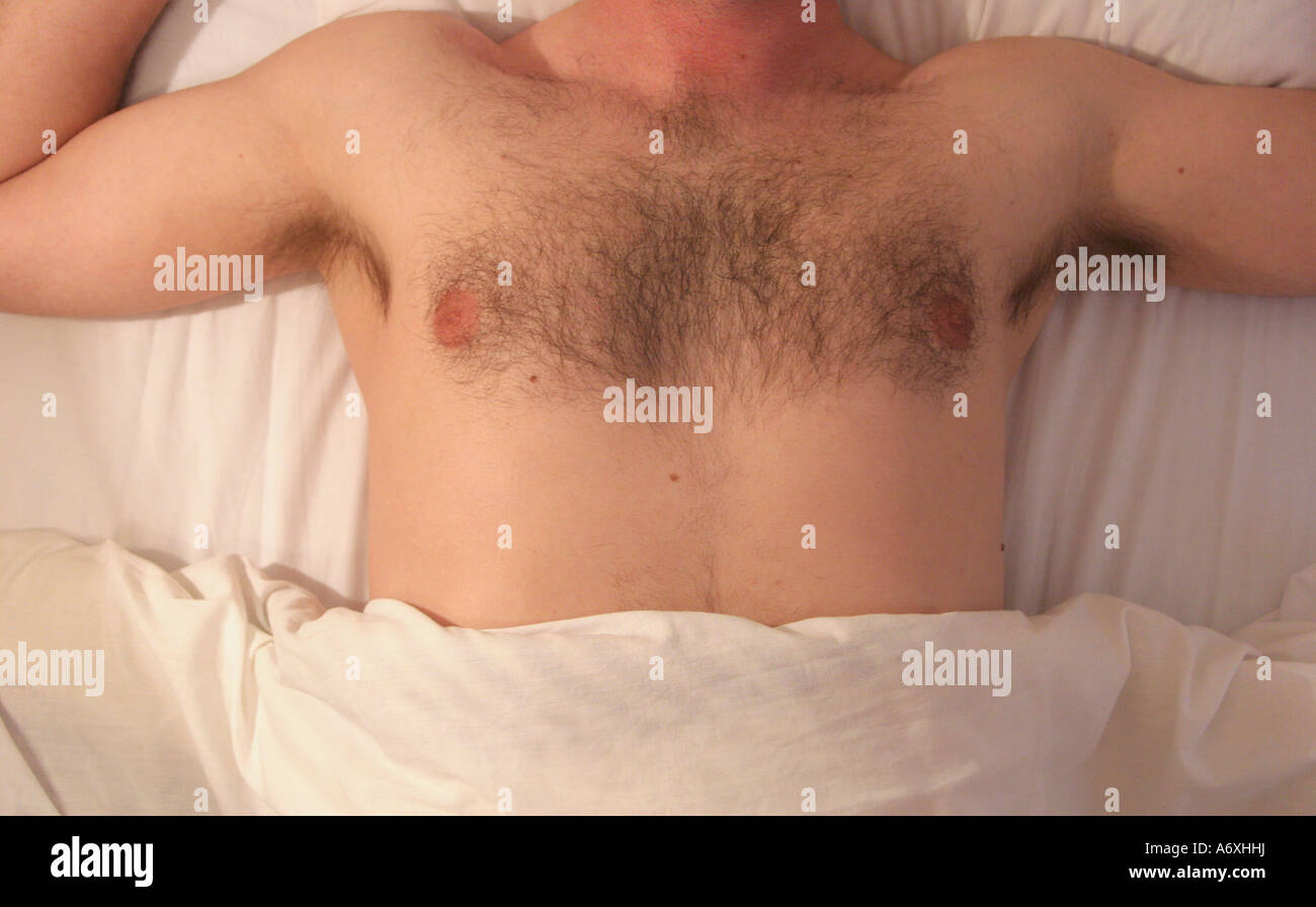 Uomo disteso nel letto rivelando hairy petto Foto Stock
