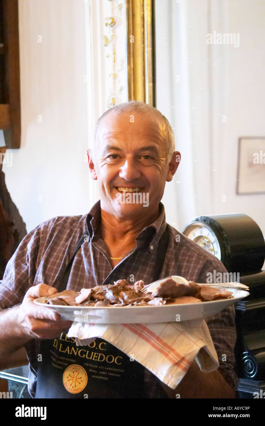 Lo zio e lo chef serve la gamba di arrosto di cinghiale. Mas de Perry, Mas Nicot. Terrasses de Larzac. Languedoc. La Francia. L'Europa. Nella sala da pranzo. Foto Stock