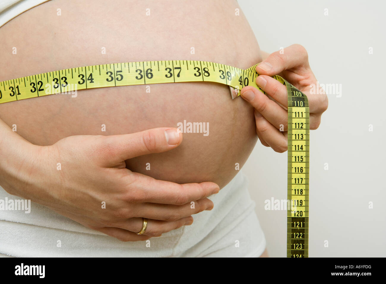 Donna incinta misurando il suo stomaco con un nastro di misurazione Foto Stock